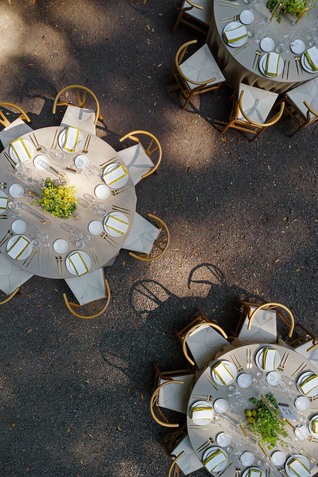 Aerial view of elegant outdoor dining tables with white tablecloths and wooden chairs arranged on a dark surface.