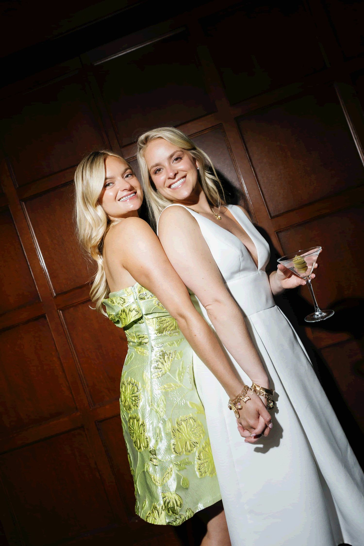 Two formal attired guests dance at a celebration, one wearing a lime green dress and one in white.