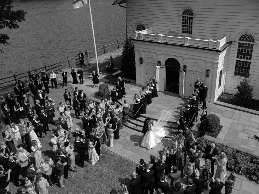 People wait in line outside a white church building in this black and white photo from a high angle view.
