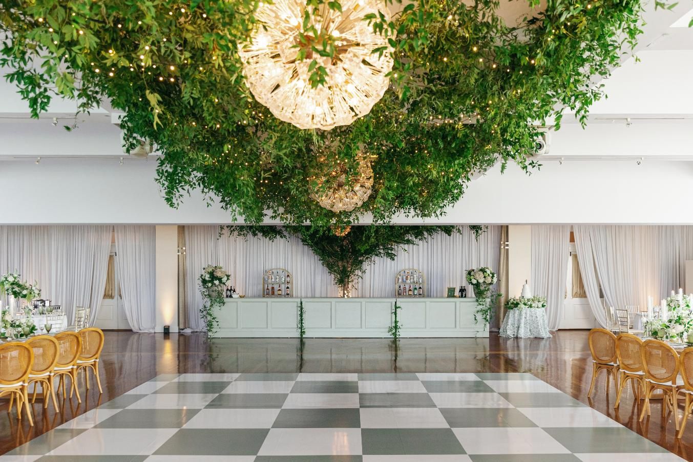 A panoramic view of an elegant event space with checkered floors and hanging greenery installations.