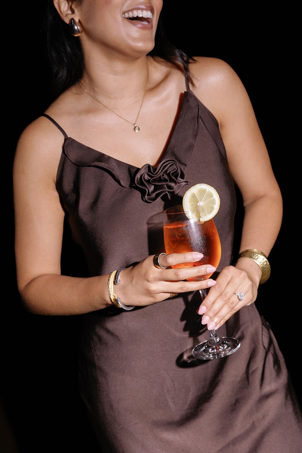 Woman in brown dress holding a cocktail garnished with lemon at an elegant event.