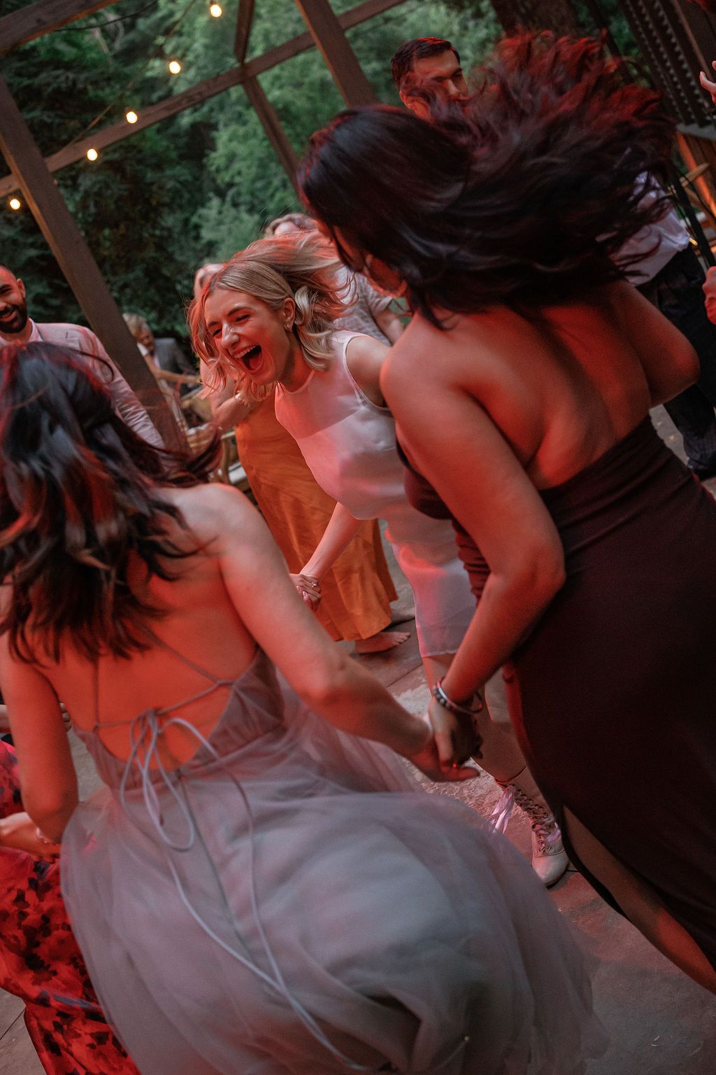 Wedding guests dancing under red lighting at an outdoor reception.