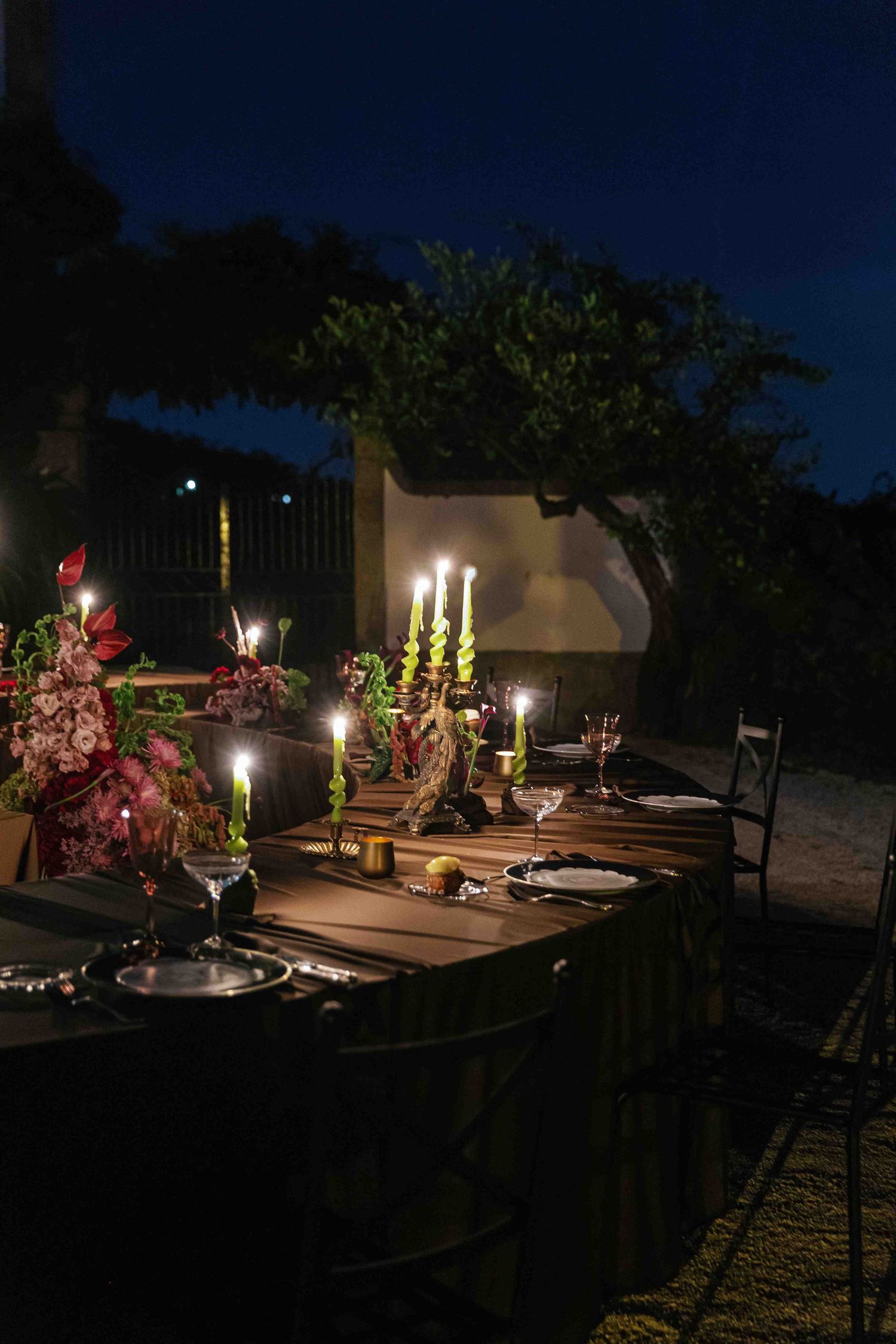 Outdoor patio area at night illuminated by warm lighting with potted plants and decorative elements creating an ambient atmosphere.