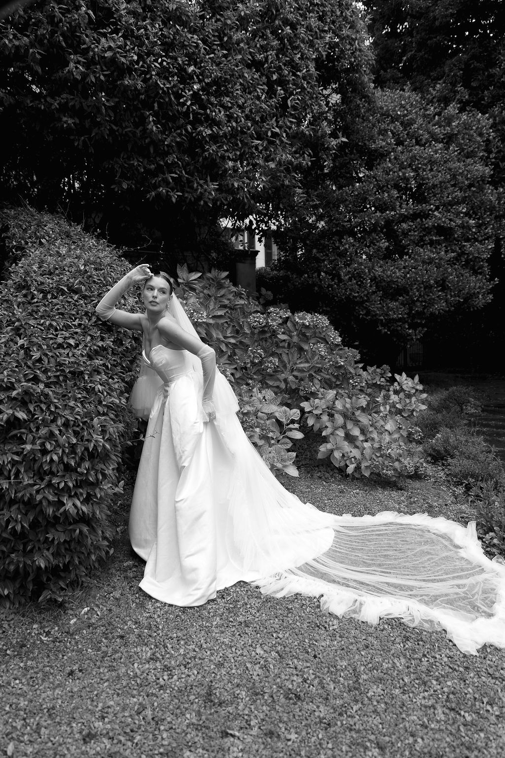 A flowing white couture wedding dress train spreads across grass in an artistic black and white composition in Lake Como.