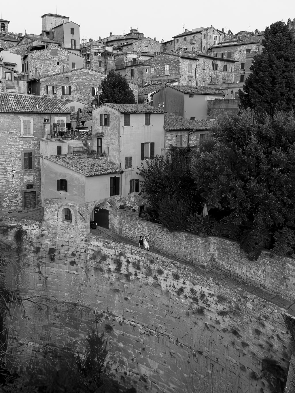 Ancient stone walls and historic buildings rise up the hillside in a medieval Italian village panorama in Tuscany, Italy.