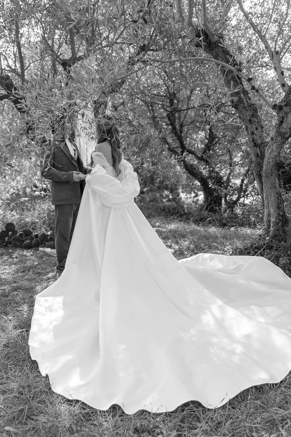 A flowing white wedding dress spreads dramatically across grass in a black and white photograph in Tuscany, Italy.
