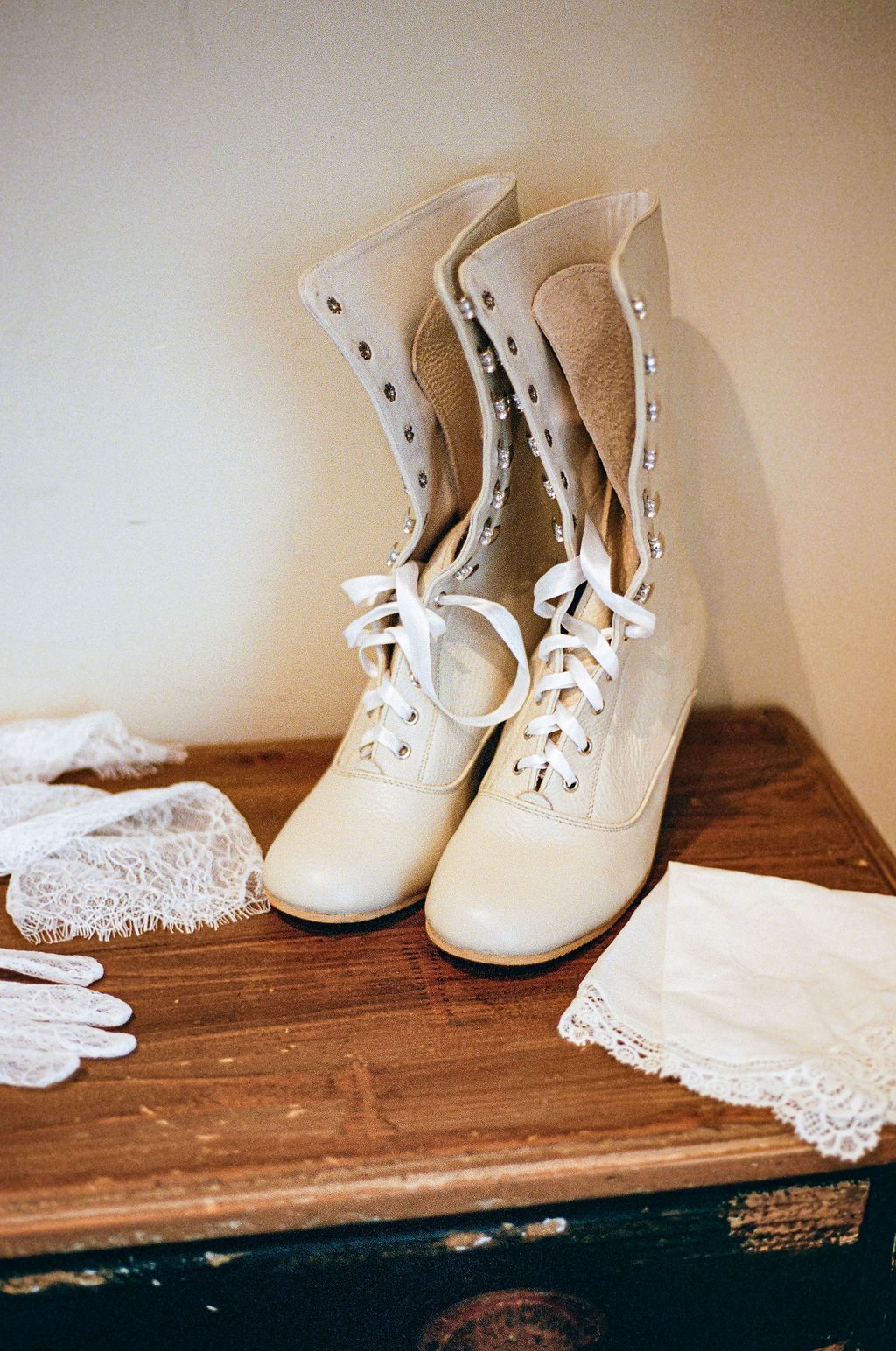 Vintage white baby shoes and lace doilies displayed on a rustic wooden surface in a soft sepia tone.