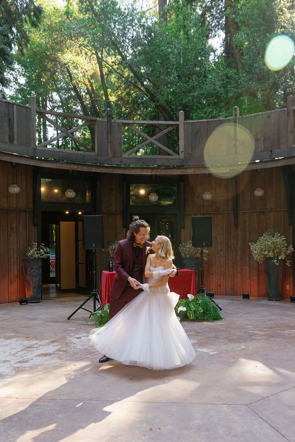 Dance floor surrounded by wooden walls and string lights where a flowing white dress twirls in motion.
