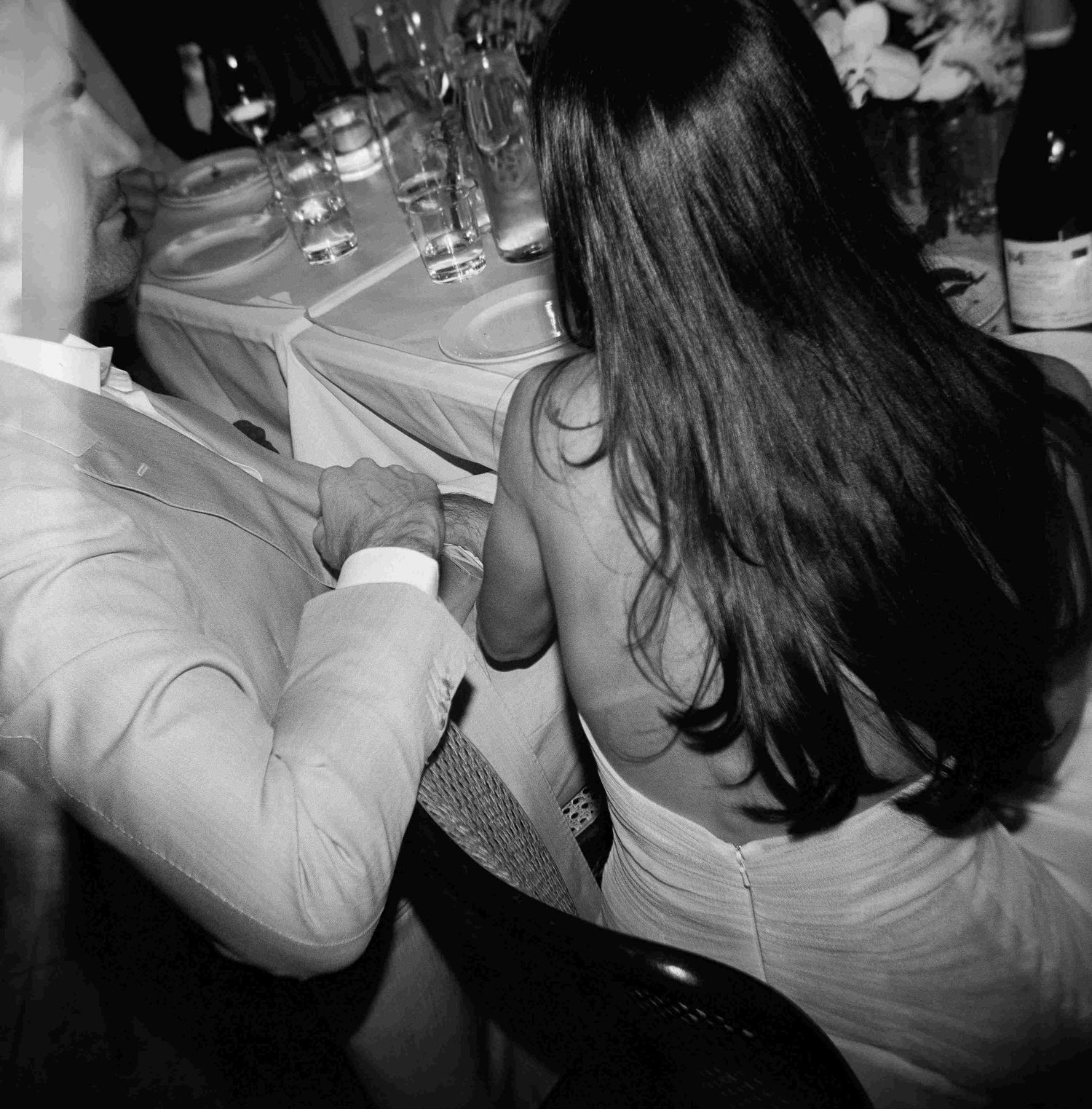Black and white photo of a couple dancing close together at a formal event with tables and wine glasses visible.