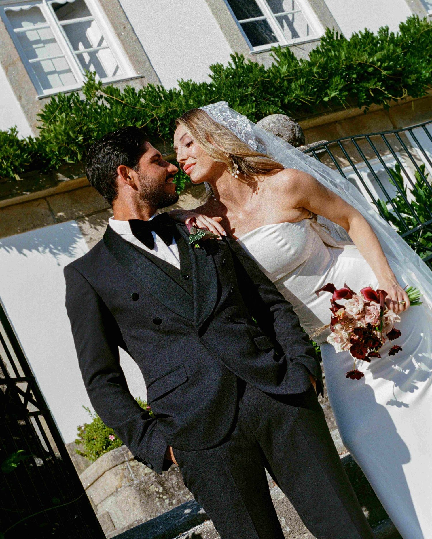 A couple shares romantic moments in a series of wedding photos against a white building with green foliage.