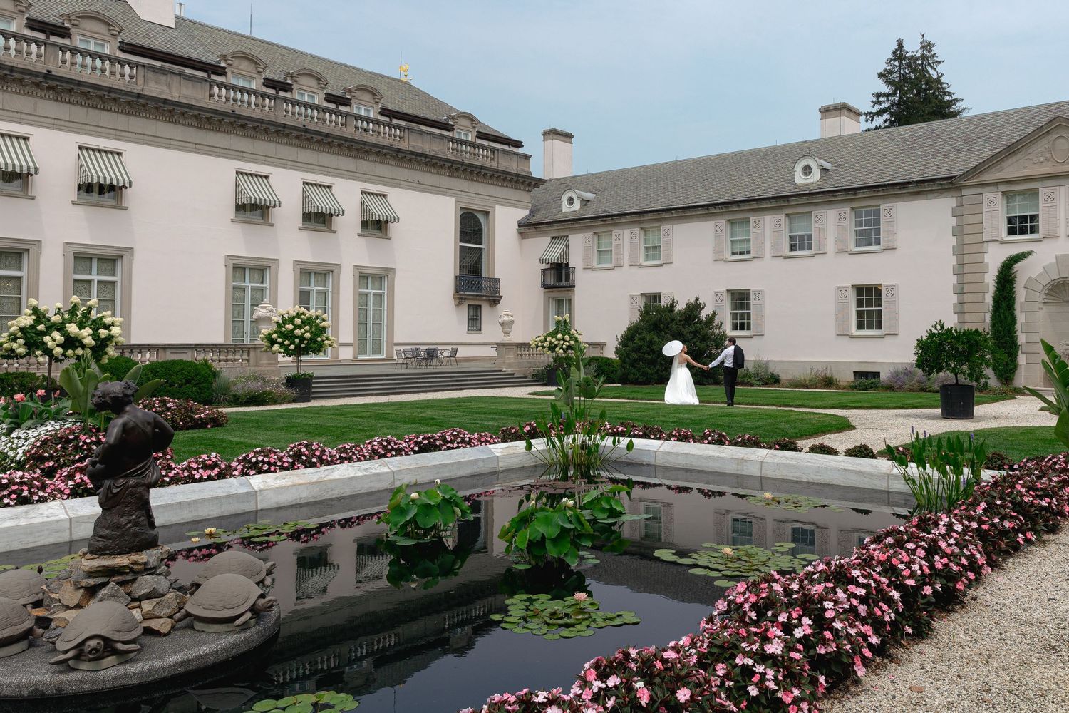 A panoramic view of a white mansion estate with manicured gardens and curved stone walls along the perimeter.