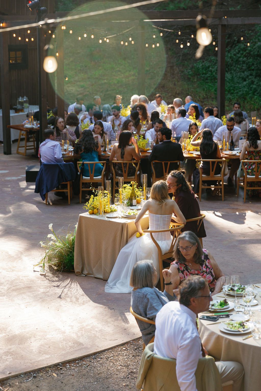 Guests dine at tables under string lights during an evening outdoor wedding reception.