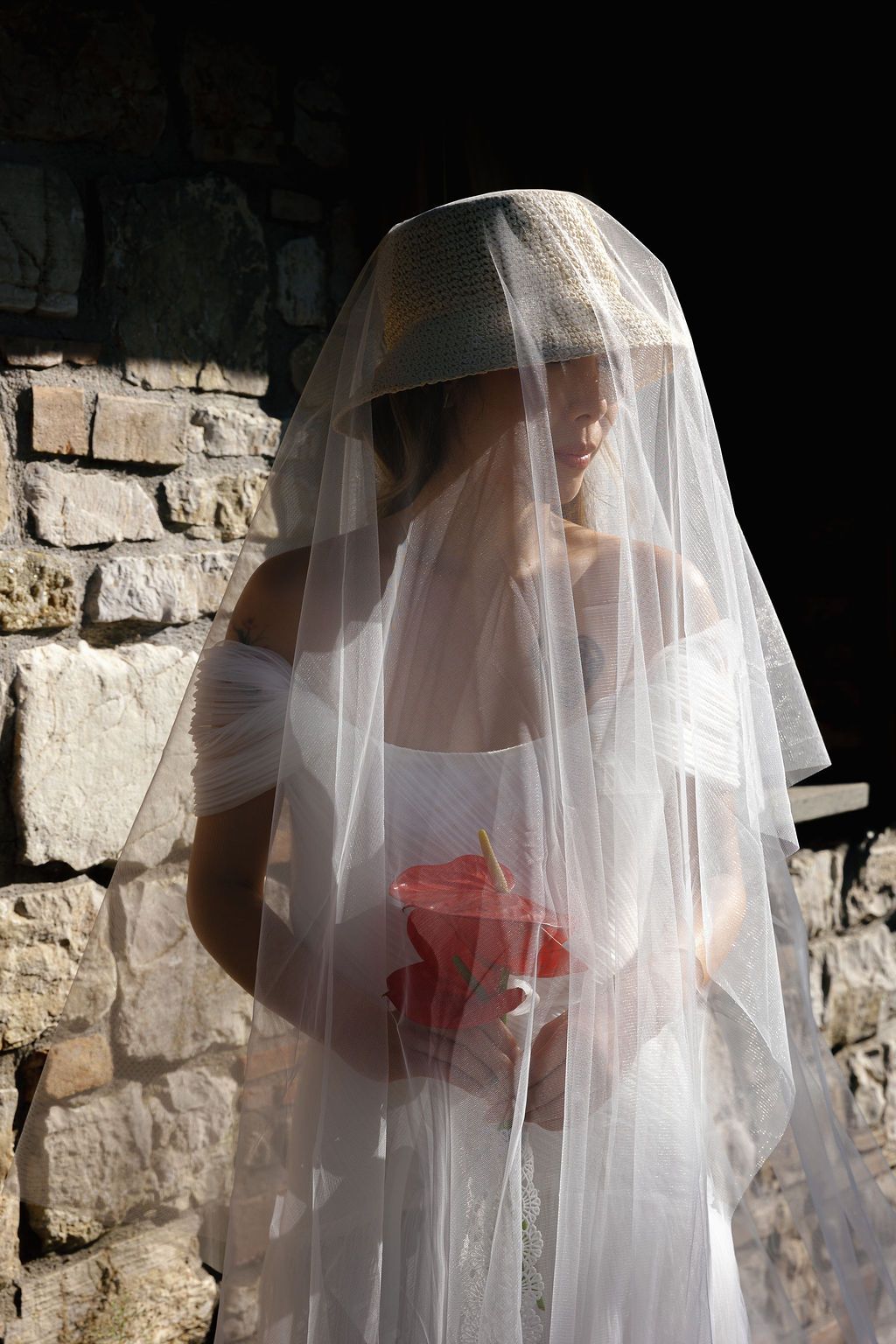 Ethereal bridal portrait with flowing white veil against a stone wall background in Tuscany, Italy.