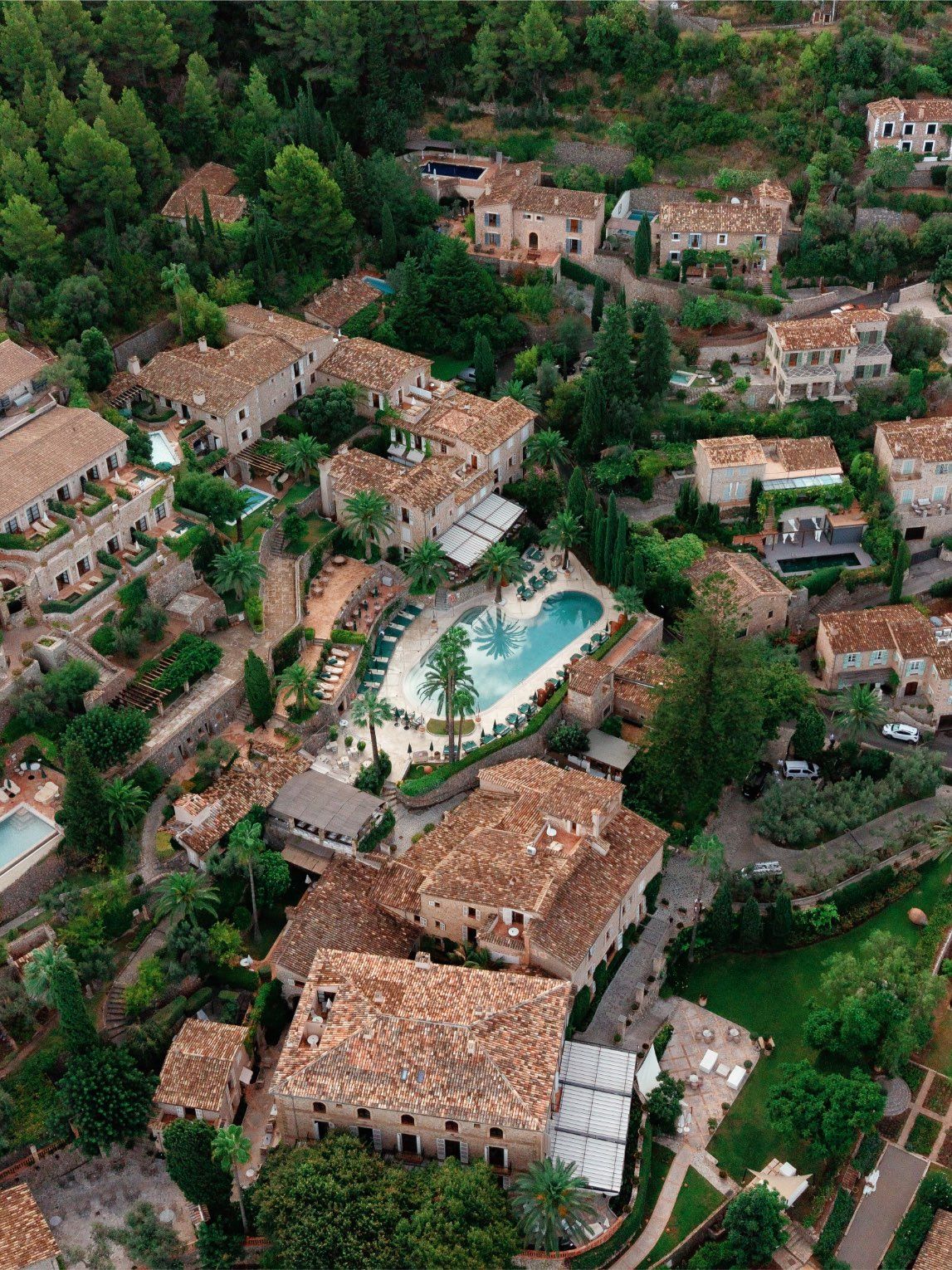 Aerial view of a Mediterranean village with terracotta rooftops, lush greenery, and a turquoise swimming pool.