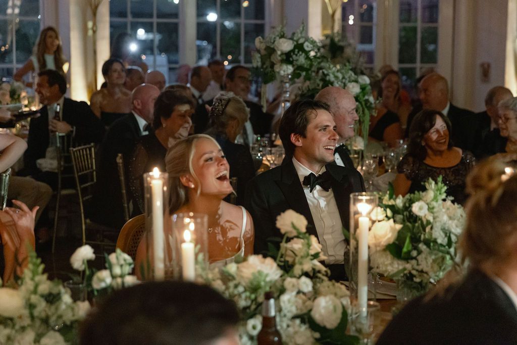 Elegant wedding reception dinner with candlelit tables adorned with white floral centerpieces and greenery.
