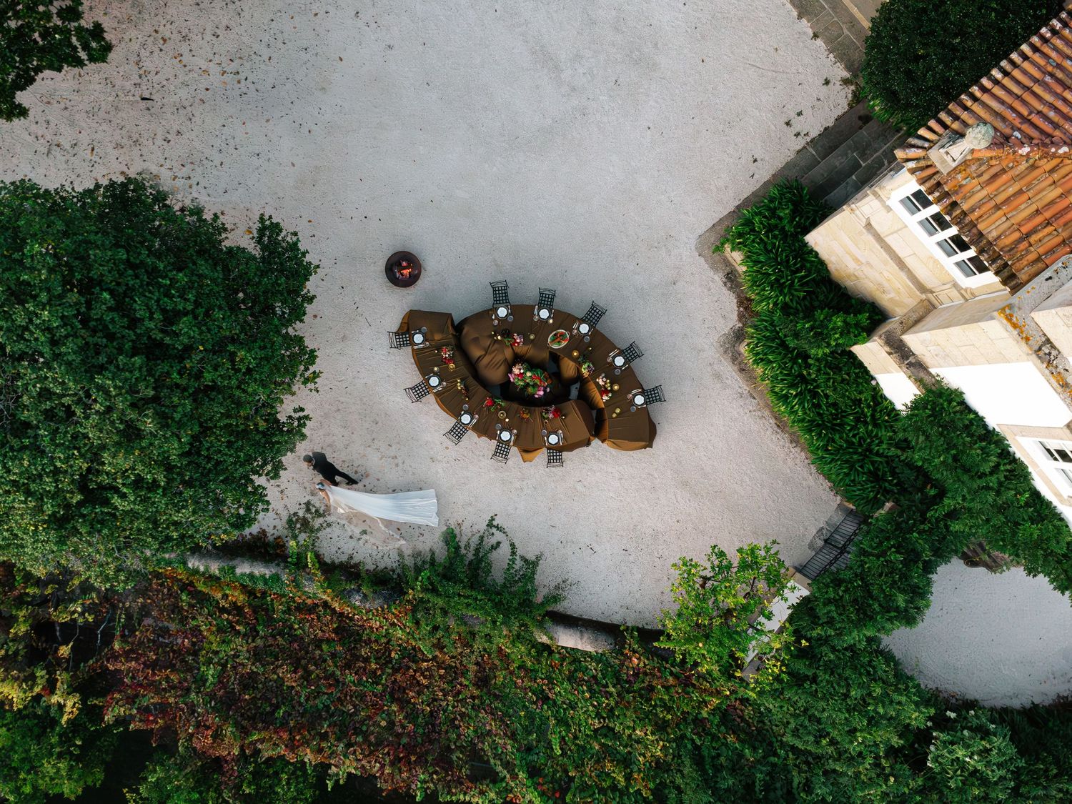 Aerial view of an outdoor patio with rustic wooden furniture surrounded by lush green hedges and trees.