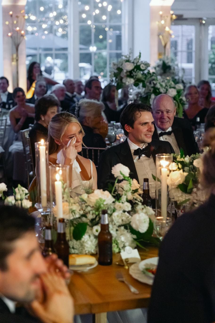 Elegant wedding reception with long tables decorated with white floral arrangements and glowing candles.