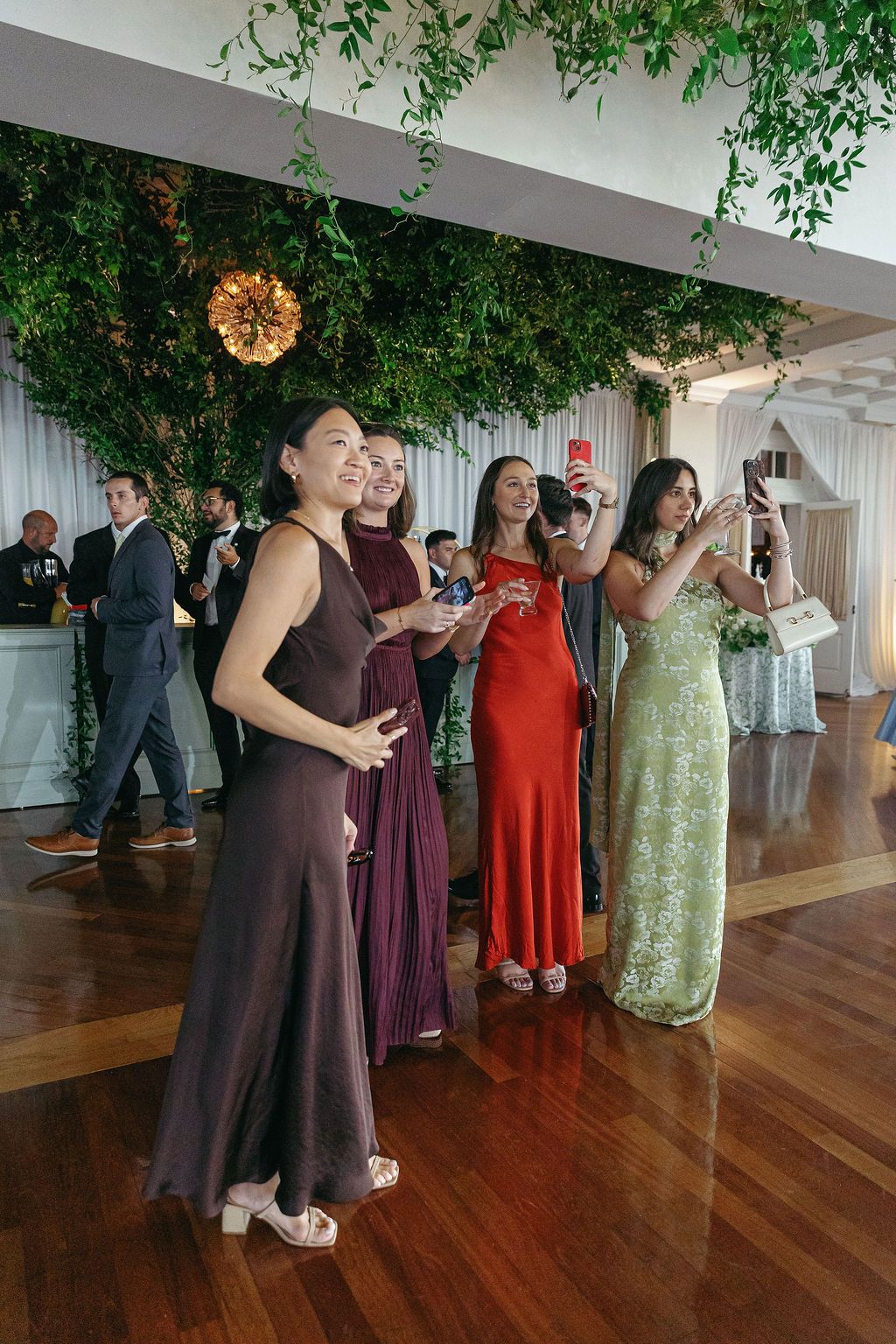 Wedding guests dancing and celebrating on wooden dance floor under decorative greenery ceiling.