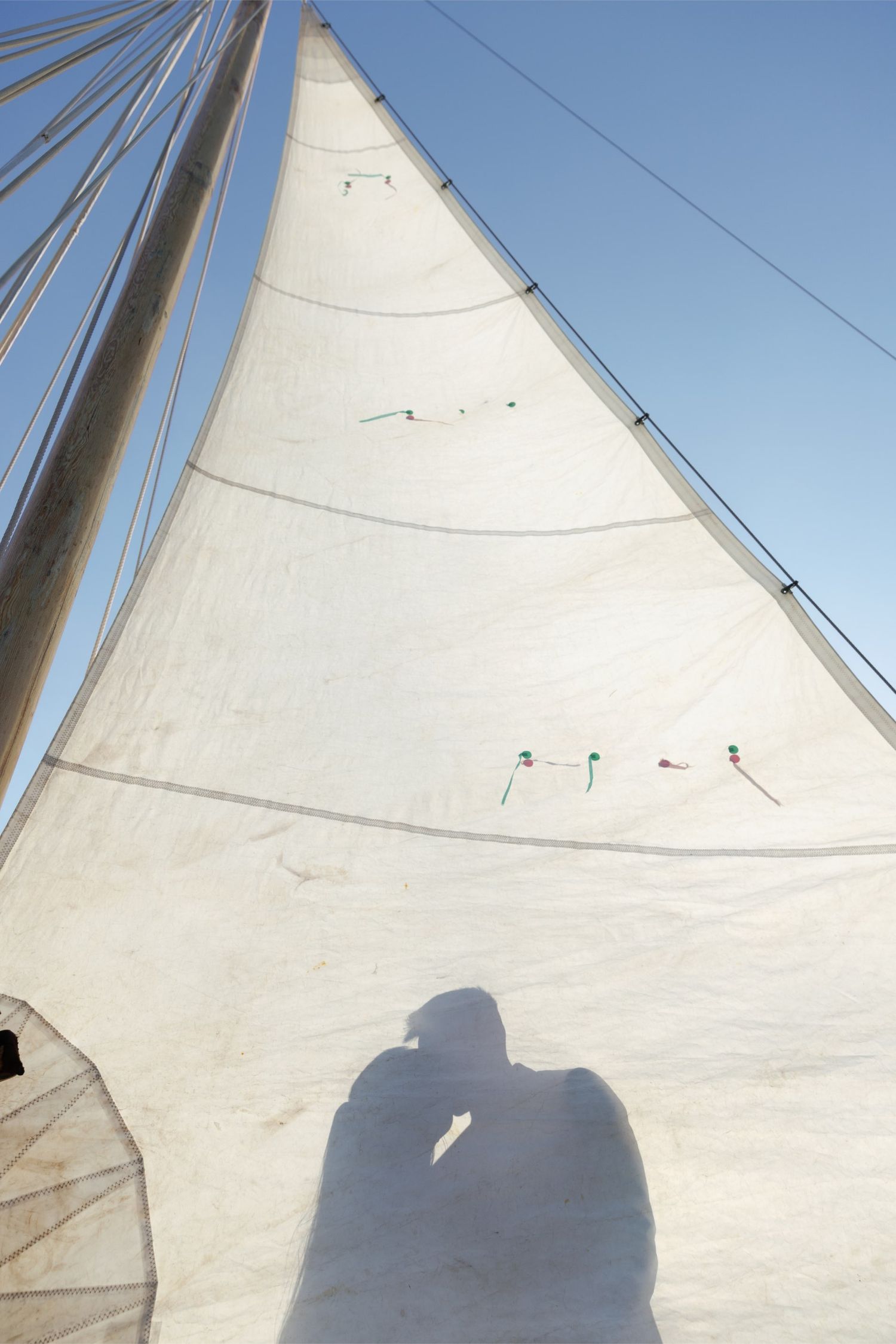 Shadow of a couple kissing cast on a white sailboat sail against a clear blue sky.