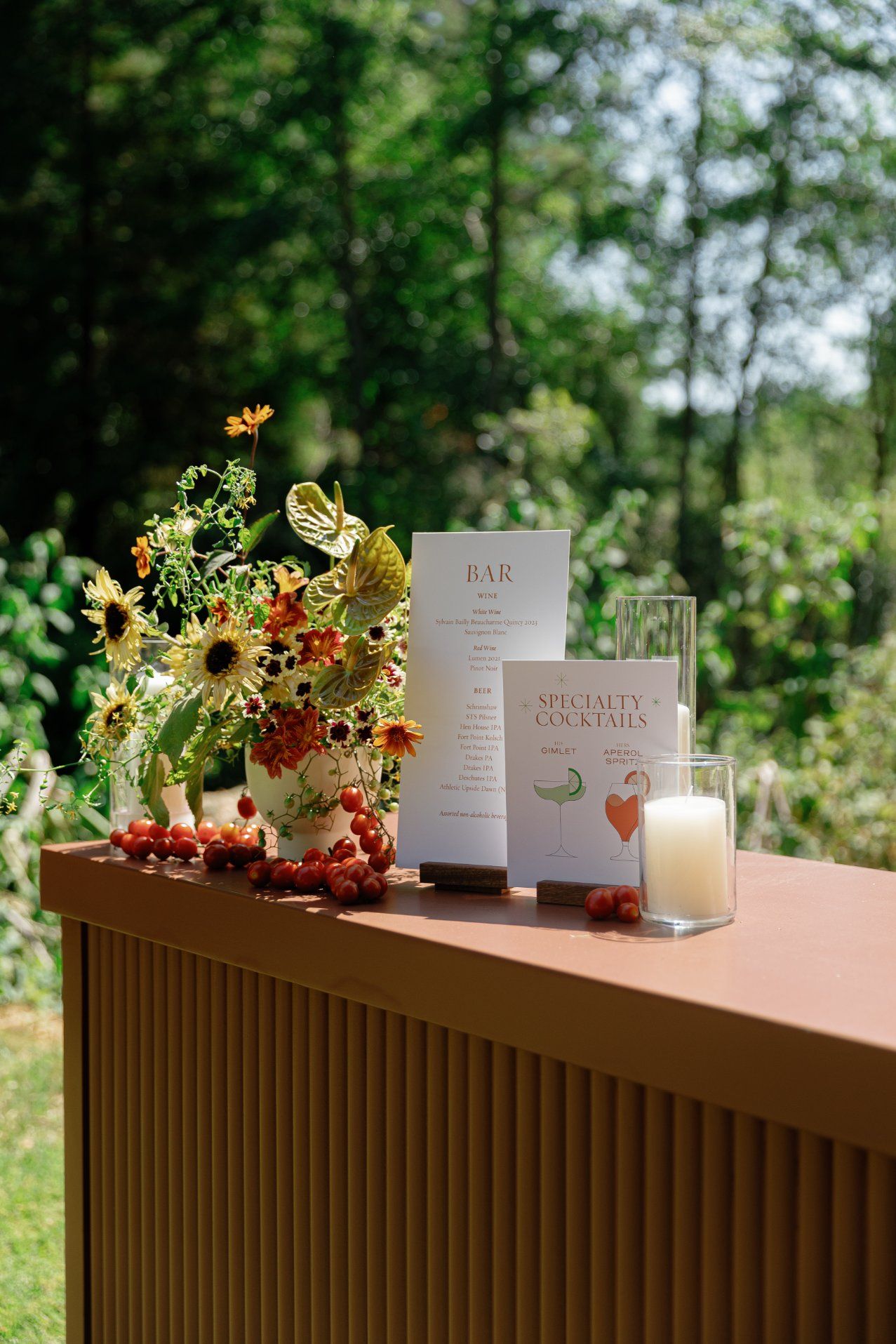 Bar setup with specialty cocktail signs and floral arrangements on a brown wooden counter.