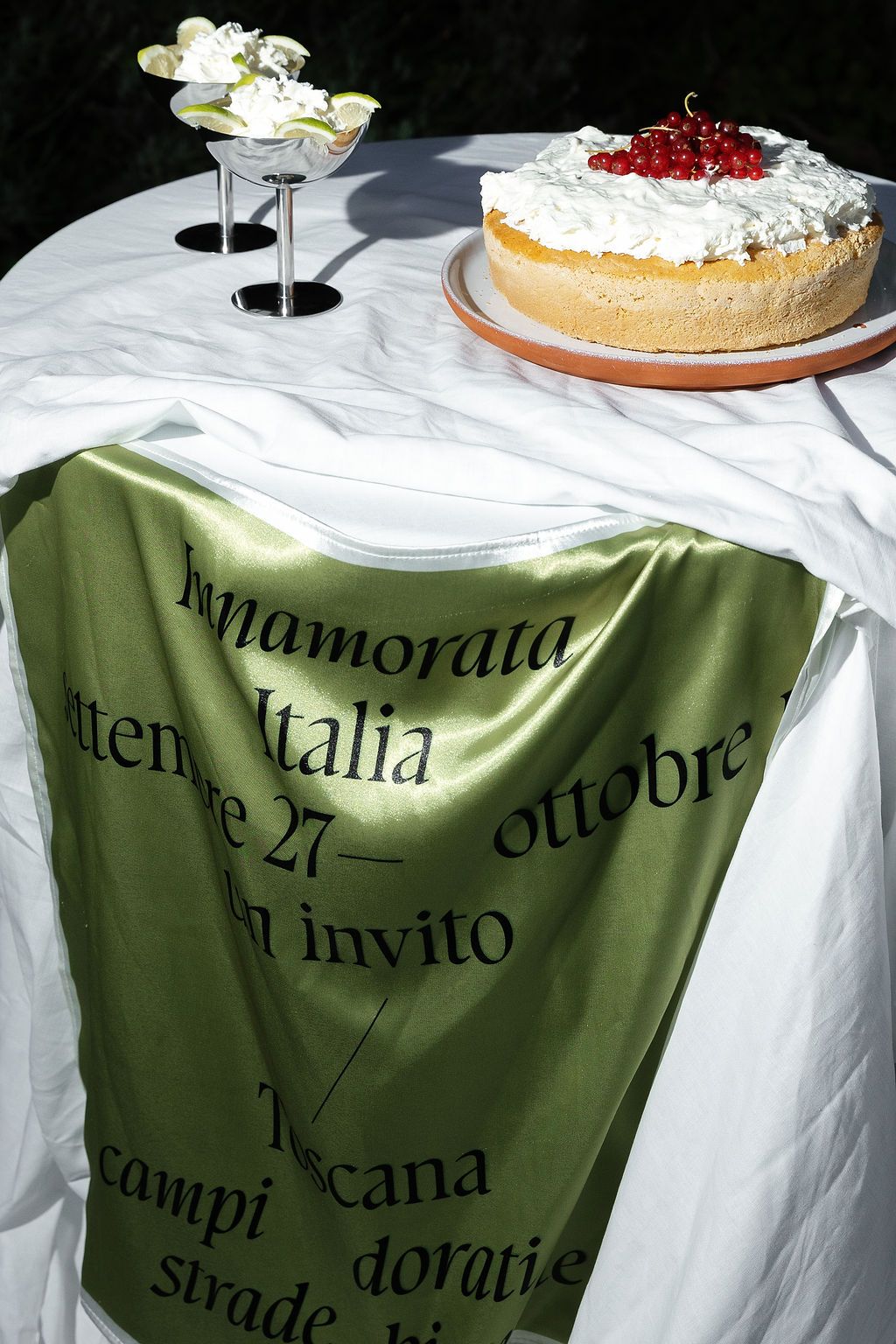 Wedding reception table with white linens, green tablecloth accents, and dessert plates displaying elegant cakes.