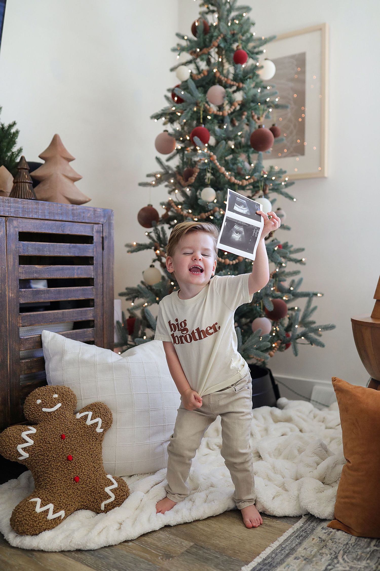 A decorated Christmas tree stands near a gingerbread pillow and wooden decor in a cozy holiday setting.