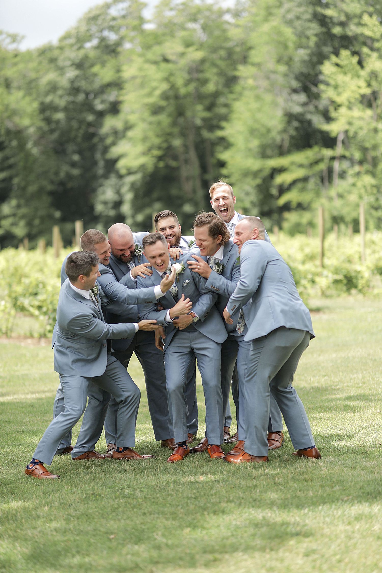 Groomsmen in gray suits playfully huddle together on grass during wedding photoshoot. Cleveland wedding photographer.