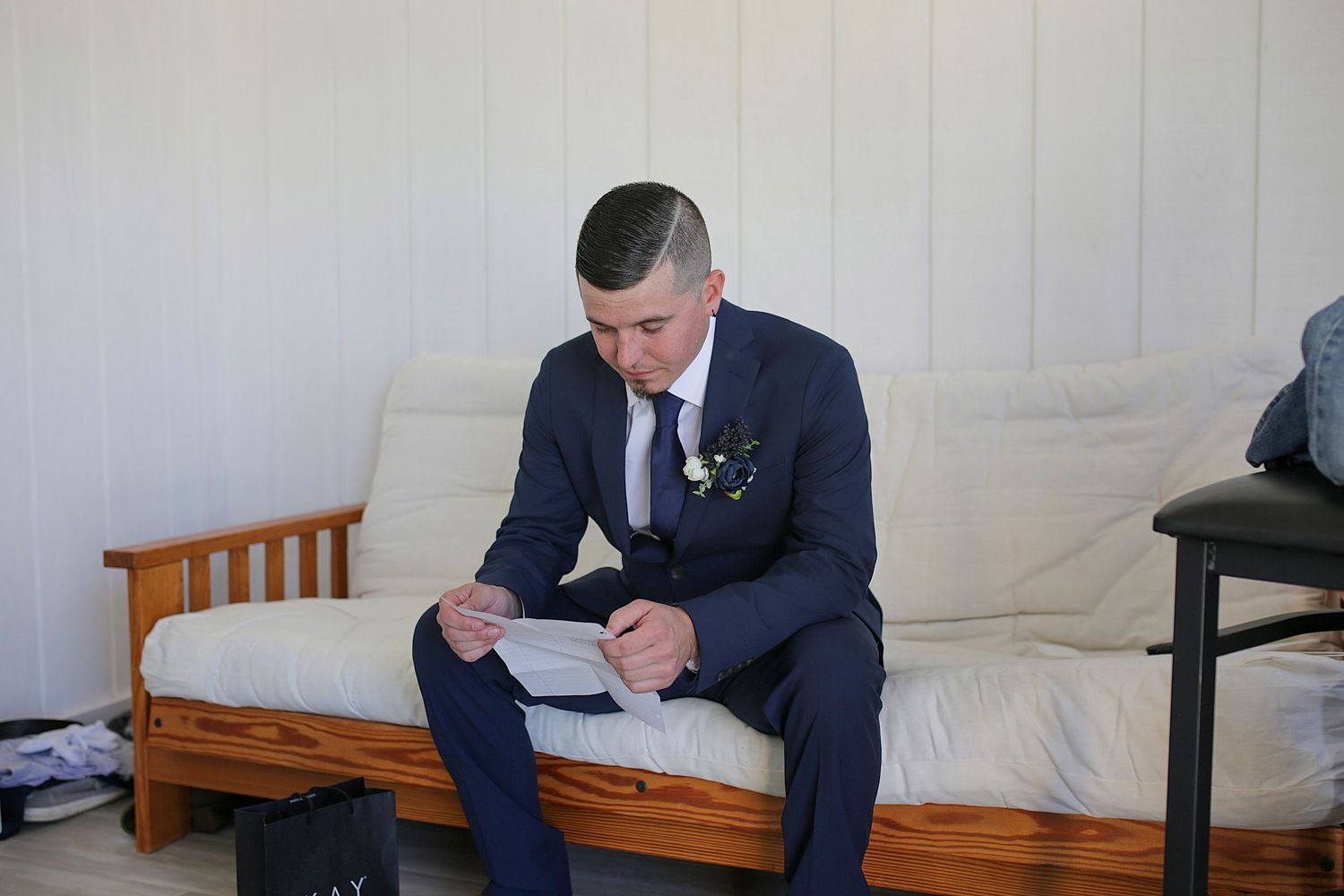 A person in a formal suit sits on a wooden bench while reading a document.