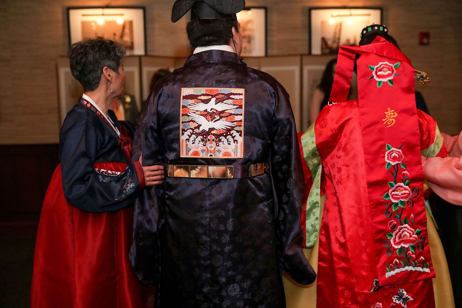 People wearing traditional Asian-style robes in black and red colors with embroidered designs gather in an indoor setting.
