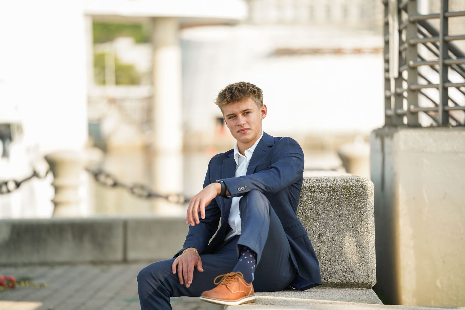 A professional in a navy blue suit sits on stone steps with a brown leather bag in an outdoor setting.
