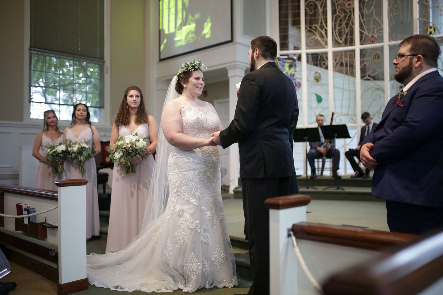 A wedding ceremony takes place in a church with attendees gathered around the altar as a couple exchanges vows.