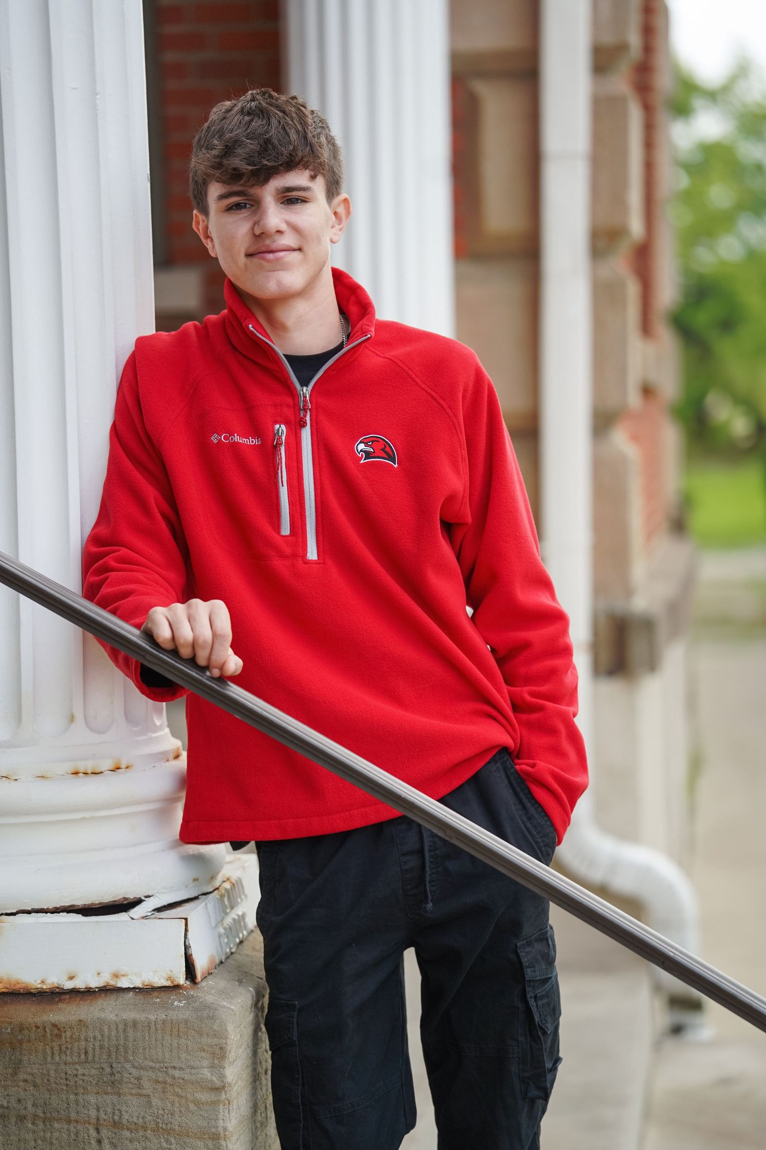 A person wearing a bright red quarter-zip fleece pullover stands on steps while holding a metal railing.