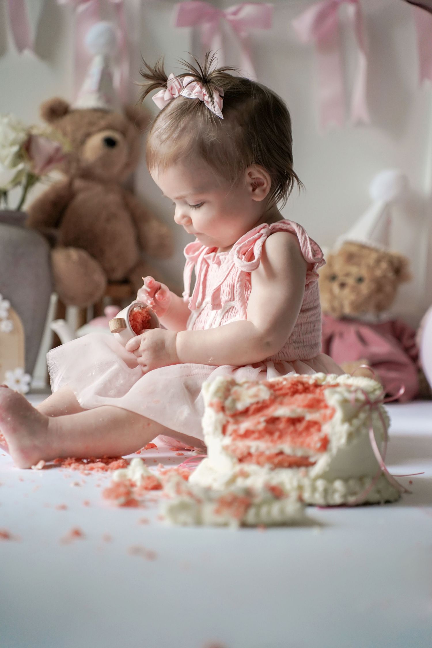 A baby in a pink dress enjoying their first cake smearing experience during a cake smash photo session.