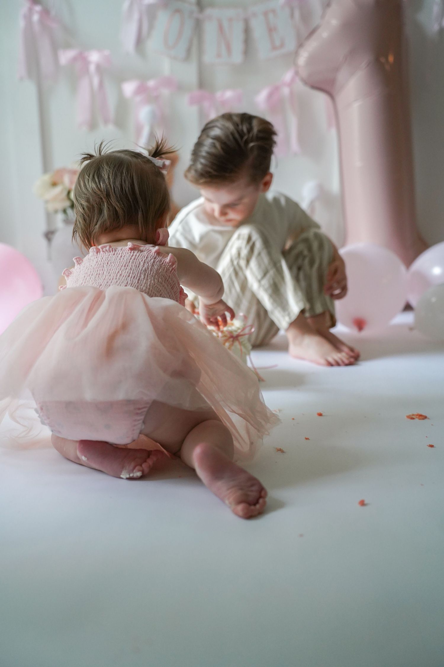 Two children playing together surrounded by pink balloons and party decorations in a soft, dreamy setting.