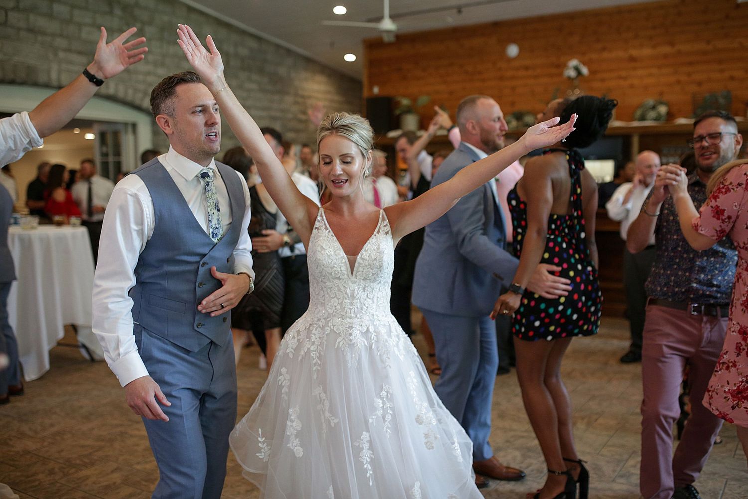 Wedding reception dance party scene with guests celebrating in rustic brick venue.