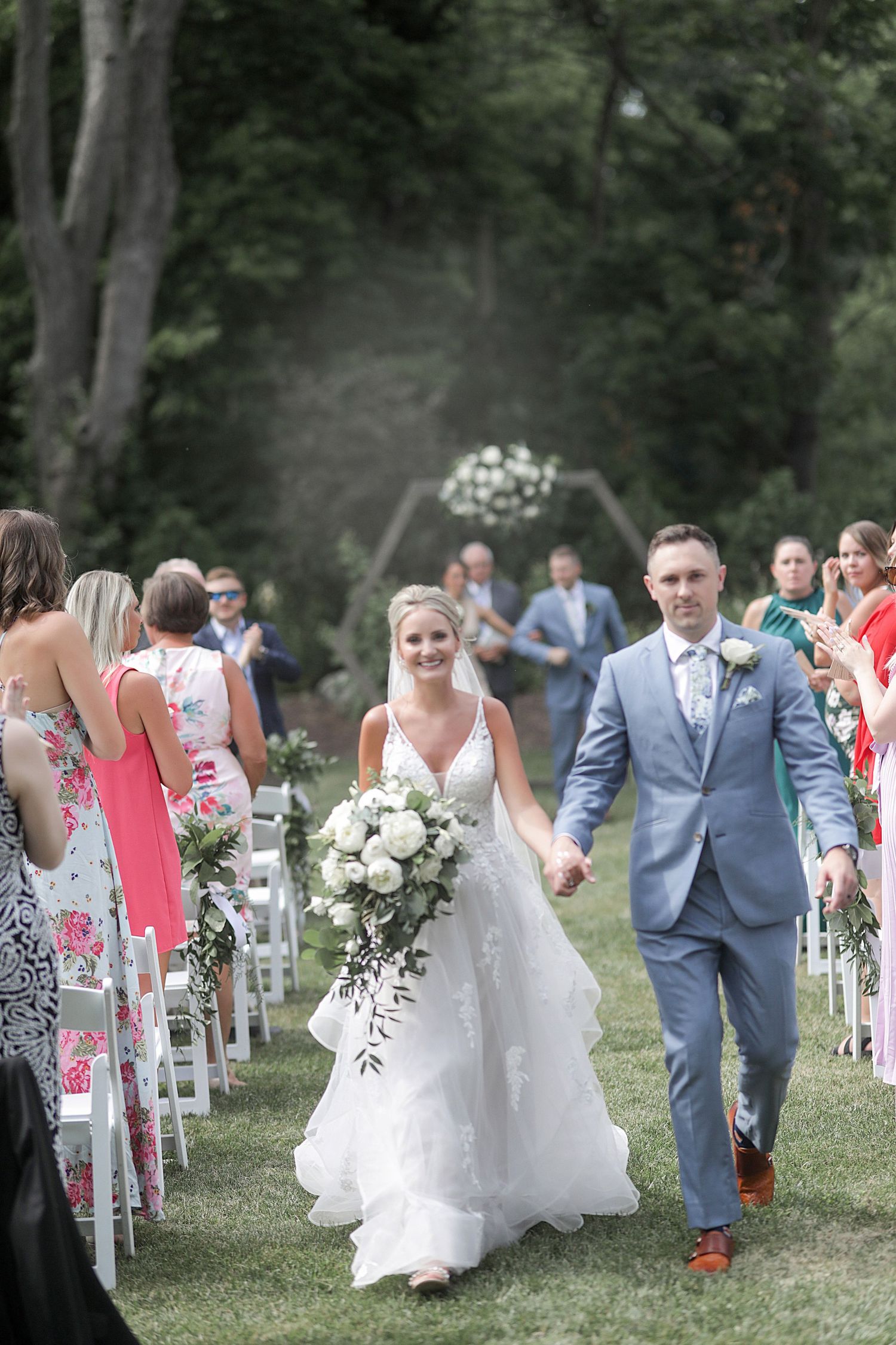 Newlyweds walking down the aisle after outdoor ceremony with floral decorations and guest seating.