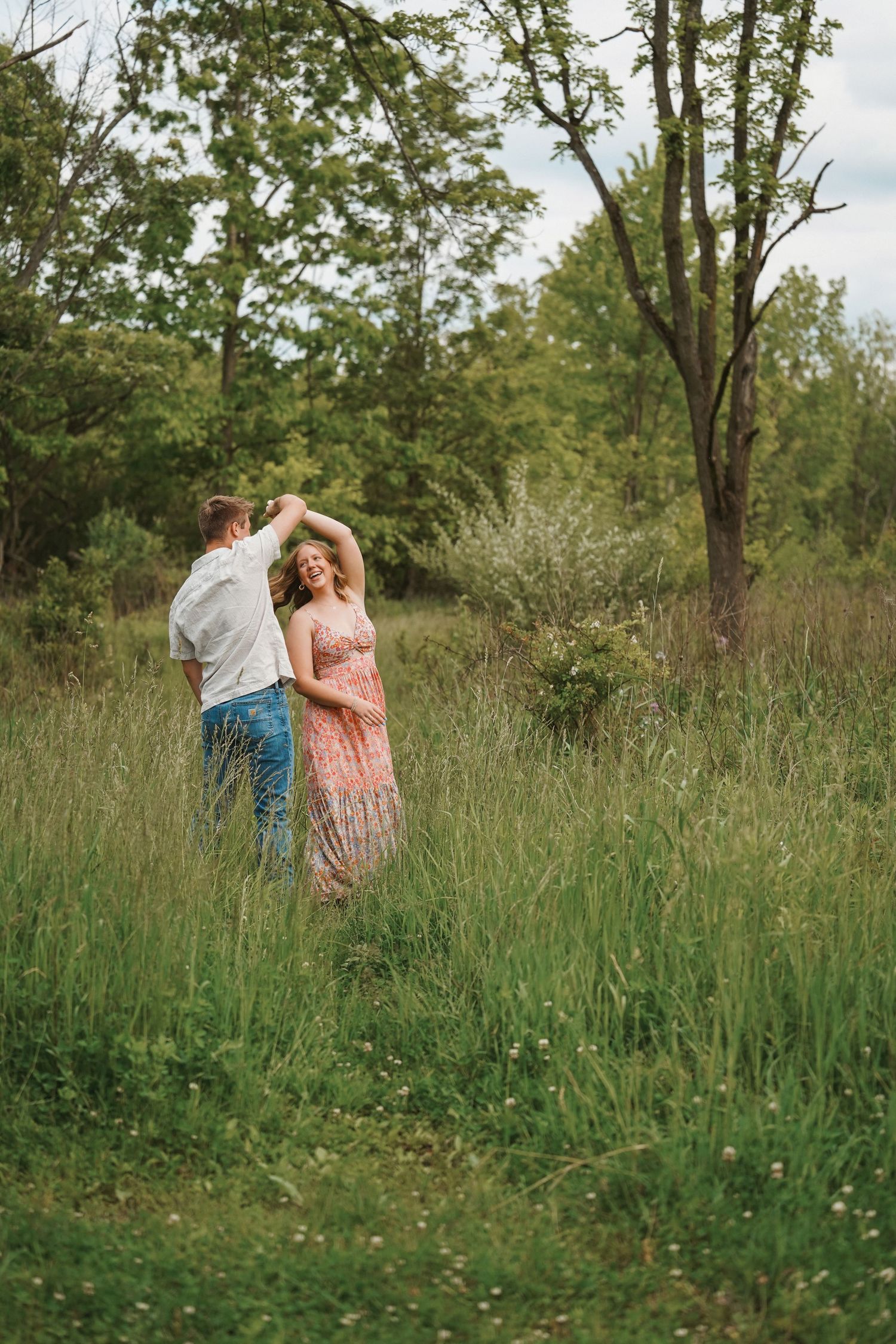 A couple dancing together in a meadow surrounded by tall grass and trees on a summer day.
