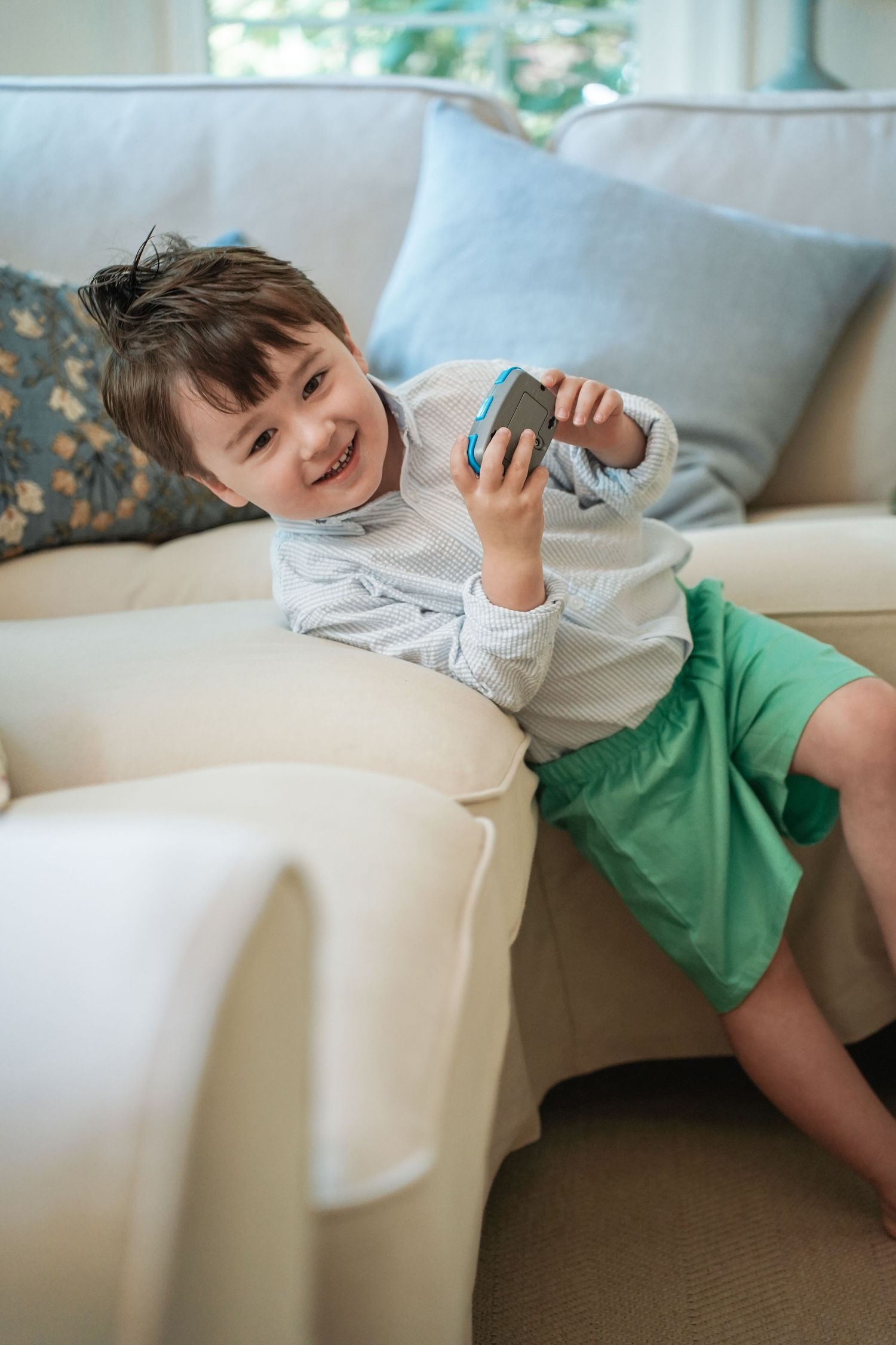 Child in white and green clothing lounges playfully on a white sofa while smiling and relaxing.