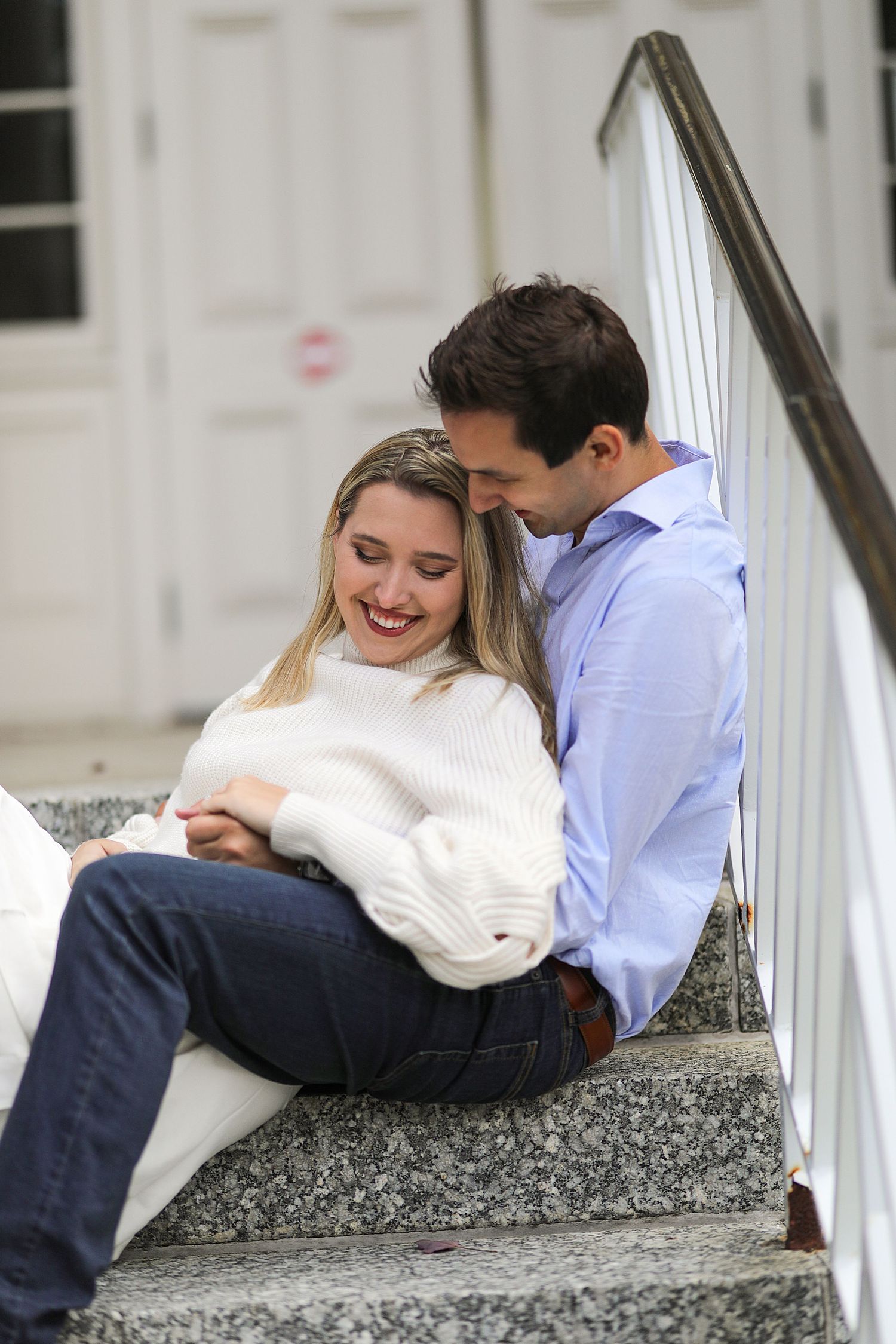 A romantic couple sits together on outdoor granite stairs, sharing an intimate moment in casual attire.
