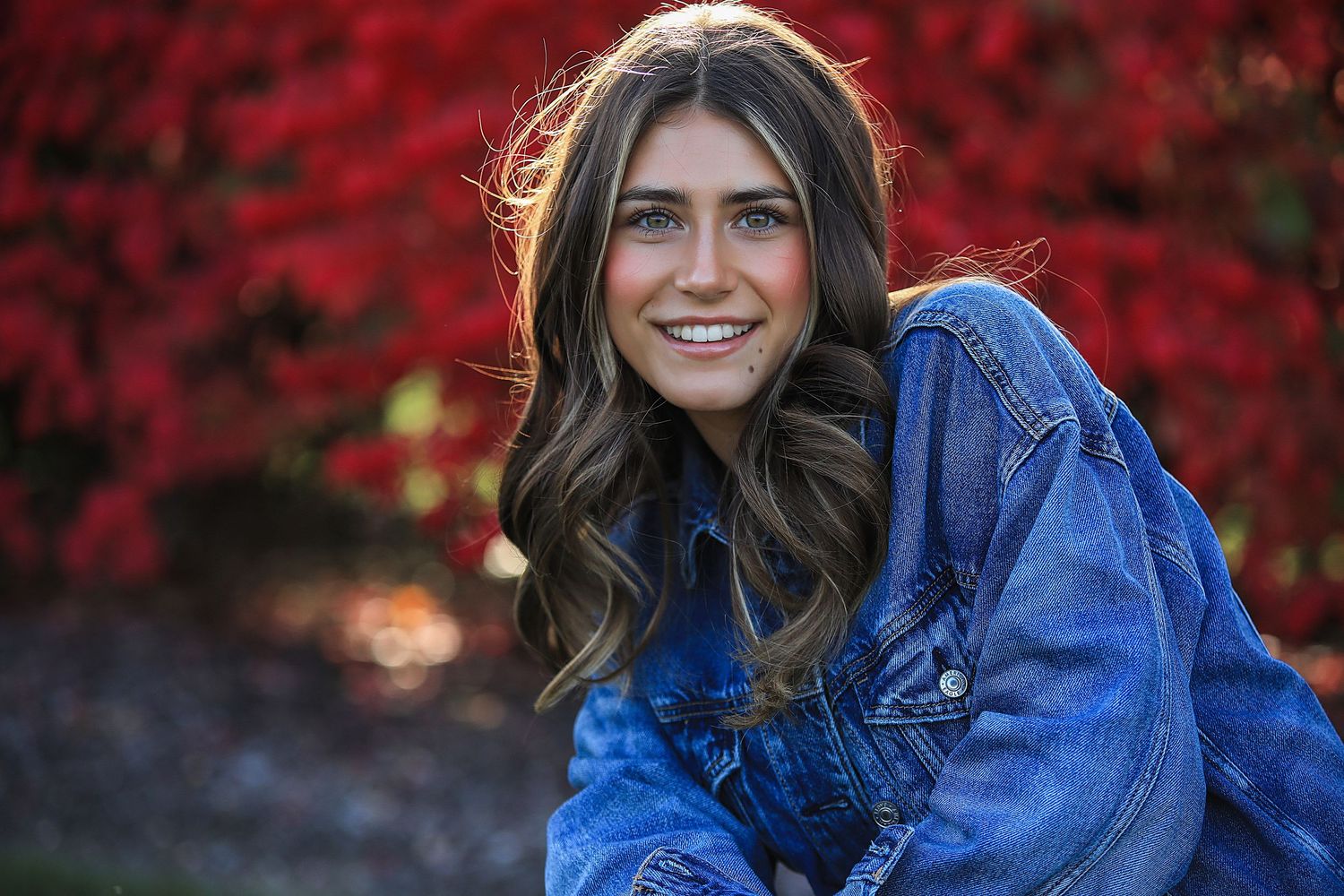 A person wearing a bright blue sweater poses against a vibrant red autumn foliage background.