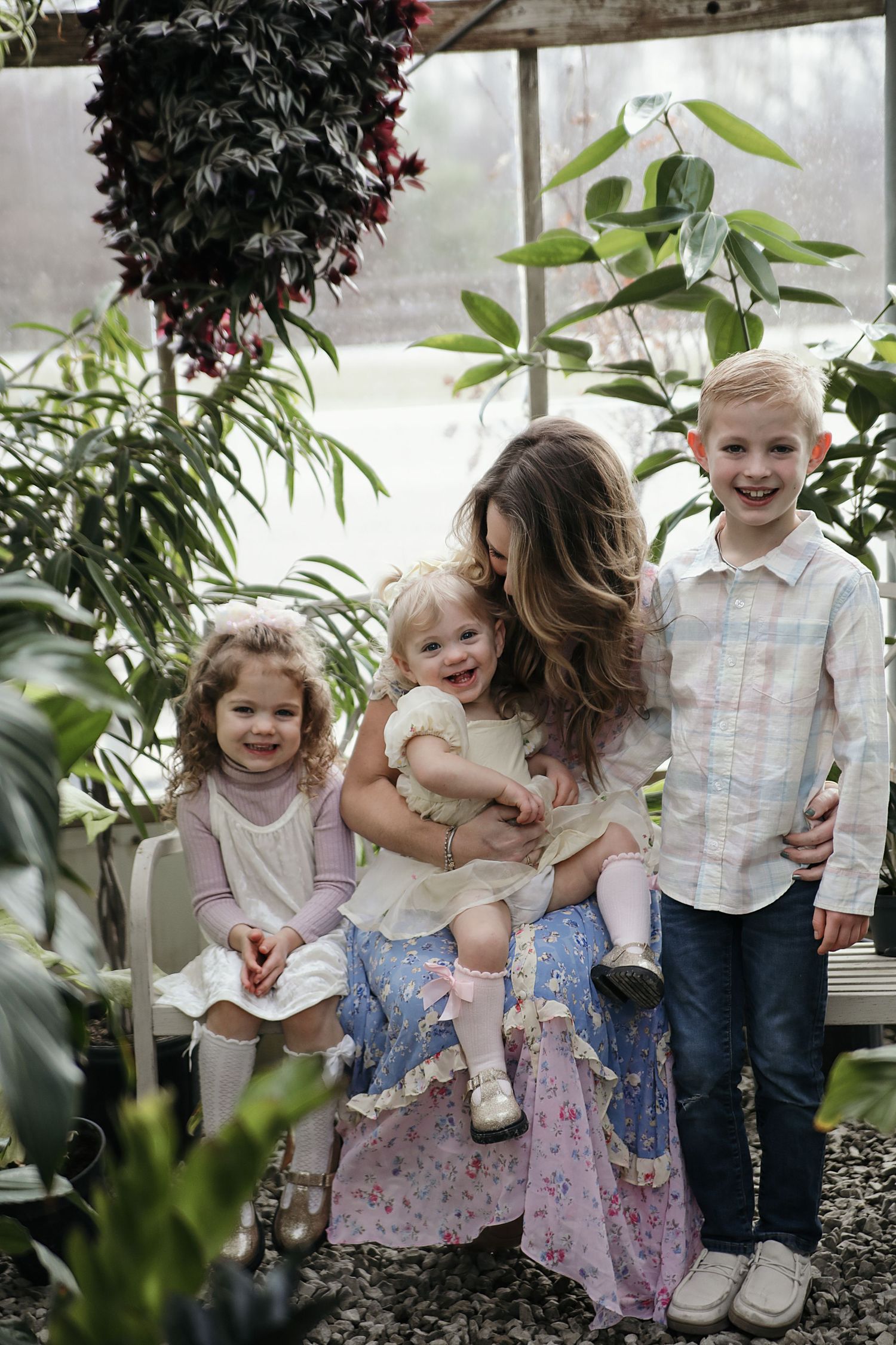 A family shares a tender moment together in a greenhouse filled with lush tropical plants and greenery.