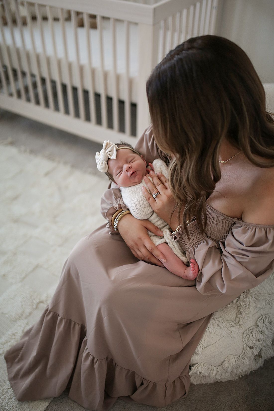 Mother in mauve dress cradling infant on white carpet. Newborn photographer Chagrin Falls, Ohio.
