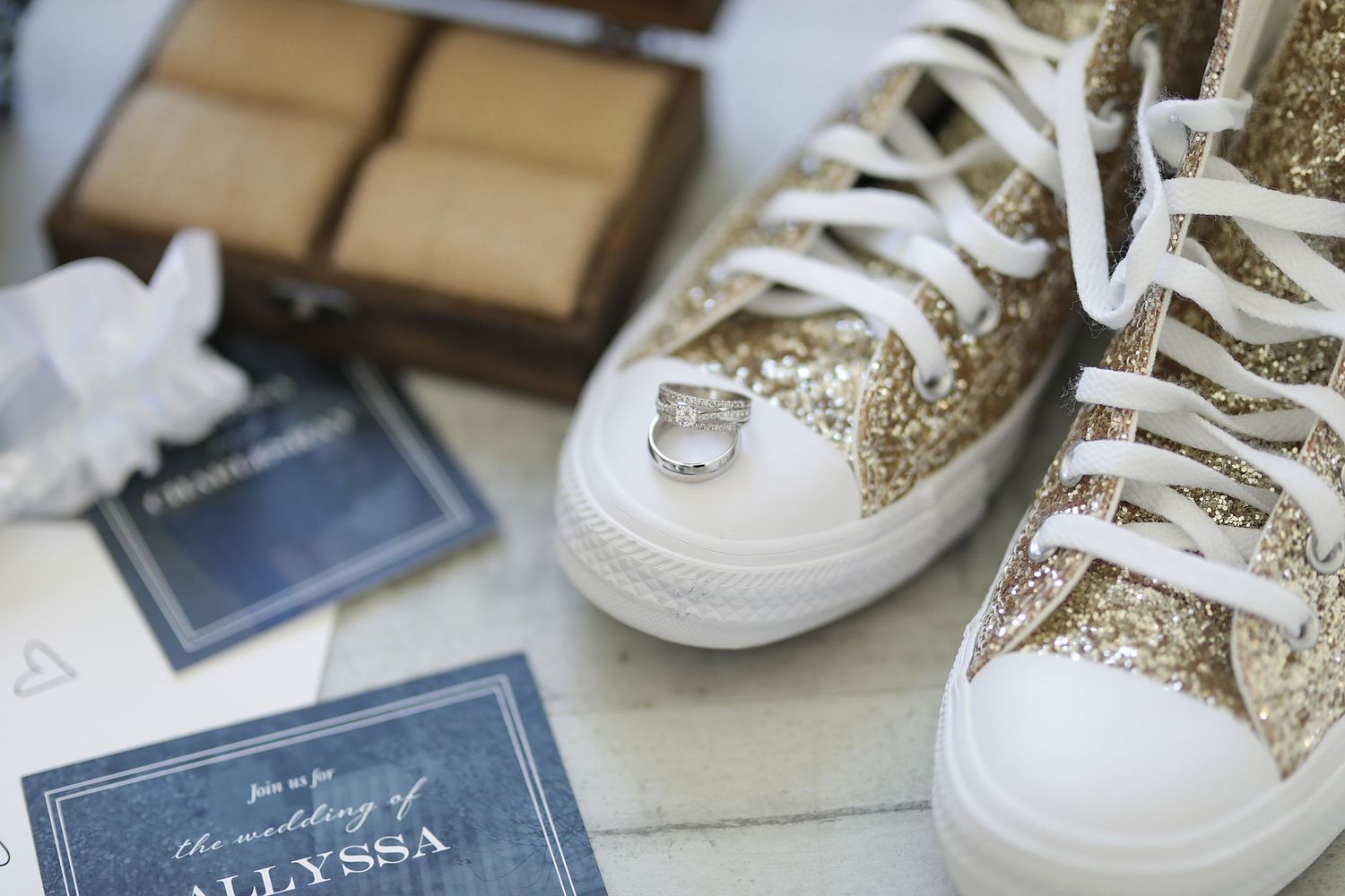 Elegant white and gold glitter wedding sneakers with matching laces arranged for a trendy bridal photo shoot.