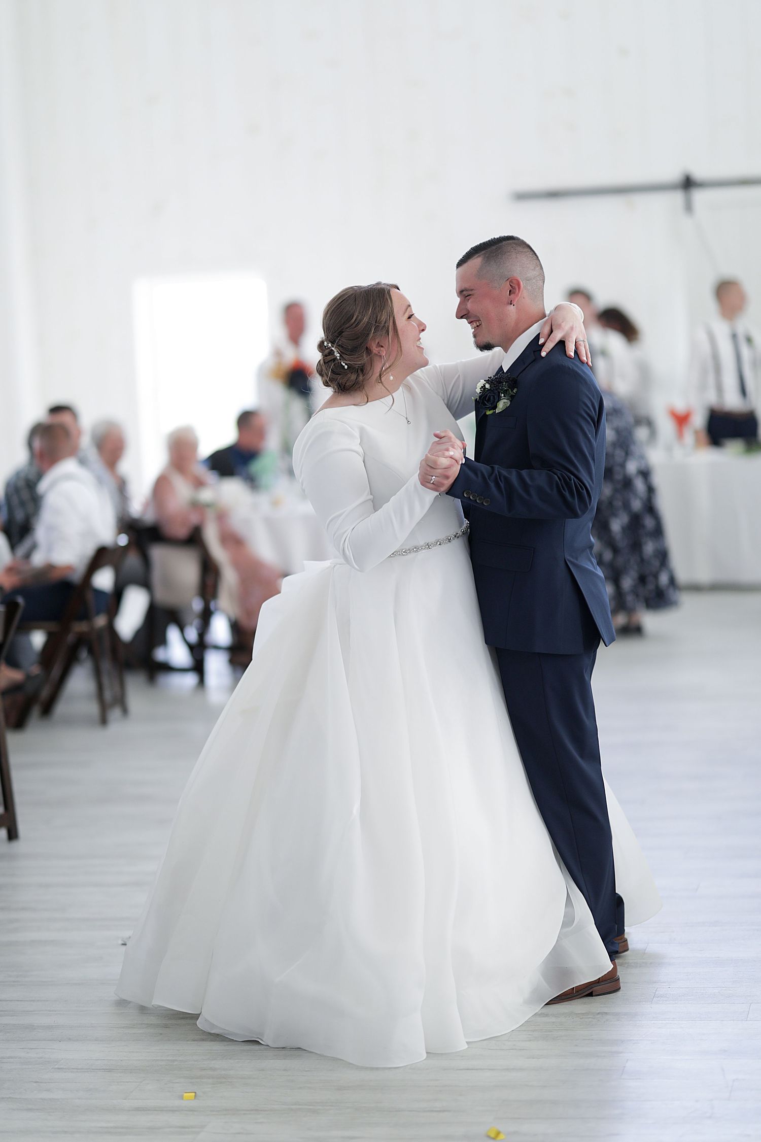 Couple shares their first dance in elegant white reception venue.