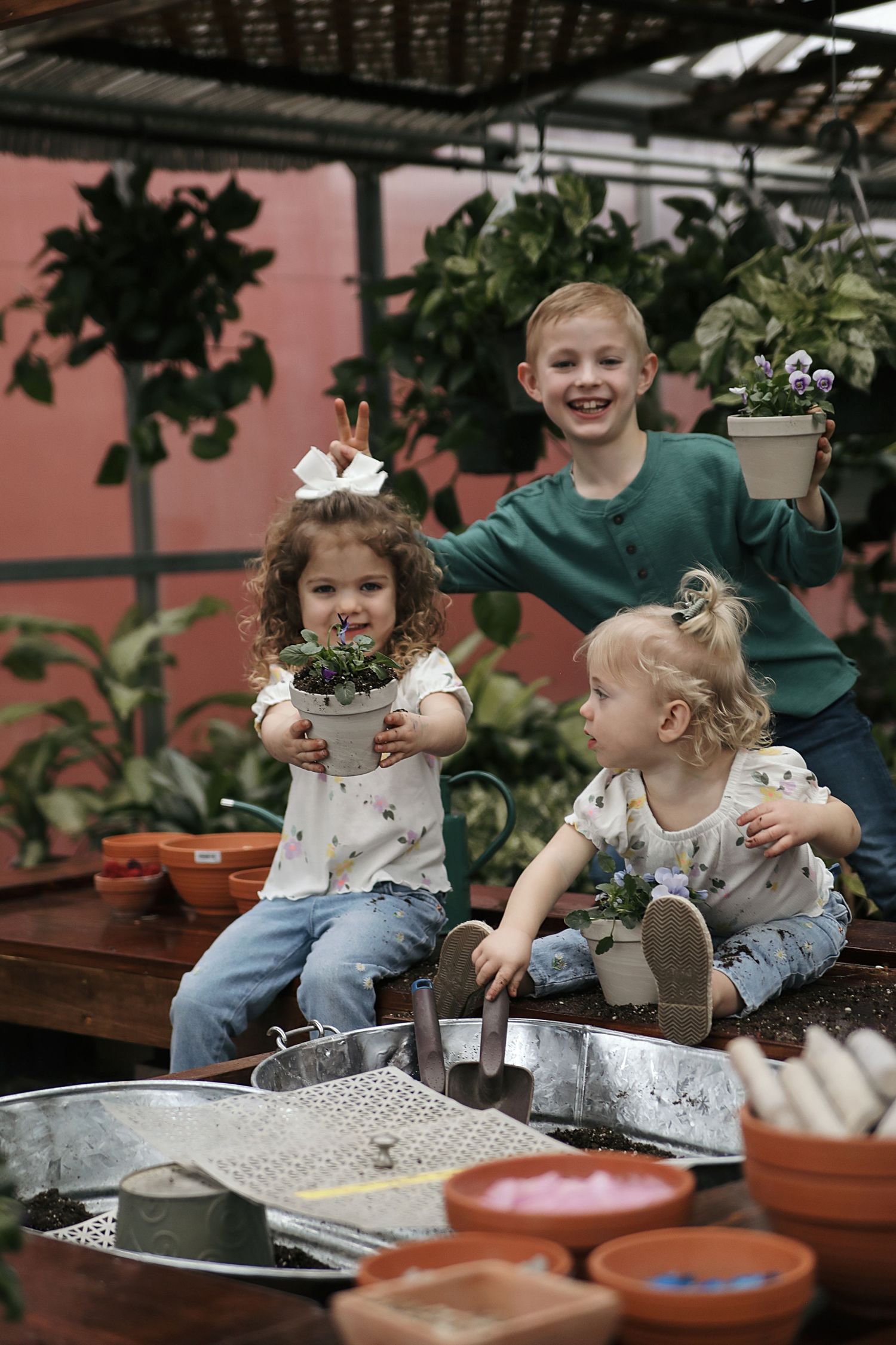 Kids sitting around a table with potted plants and gardening supplies during an indoor planting activity.