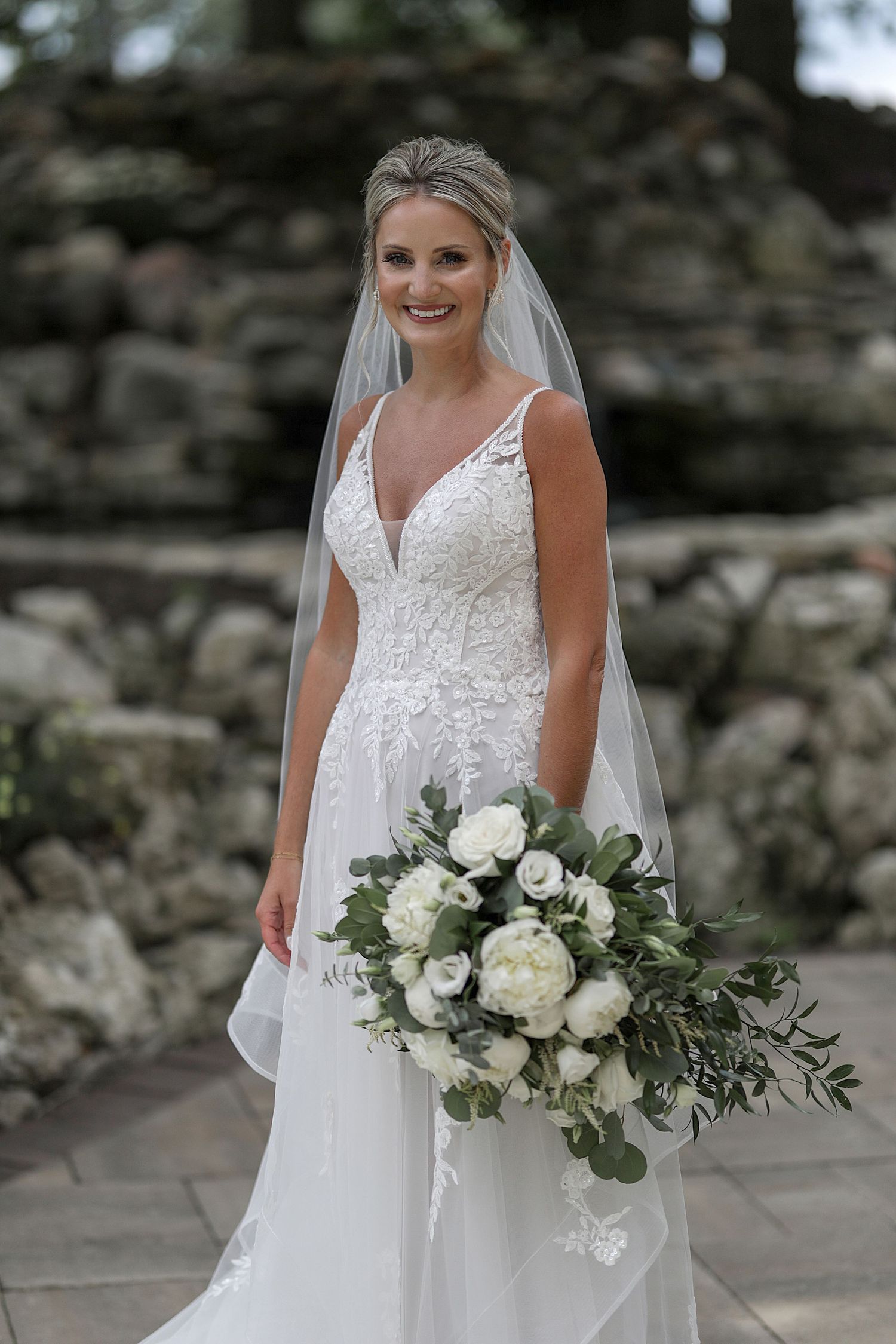 Wedding portrait featuring elegant white bouquet and lace bridal gown against stone backdrop.