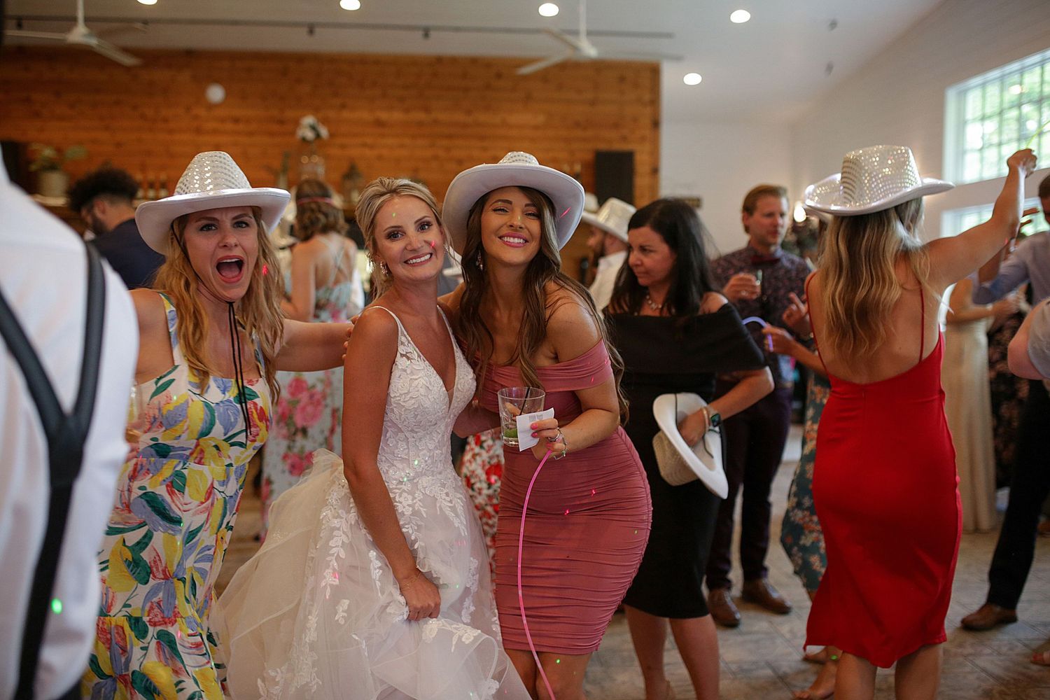 Wedding guests in colorful dresses dance and celebrate at a reception.