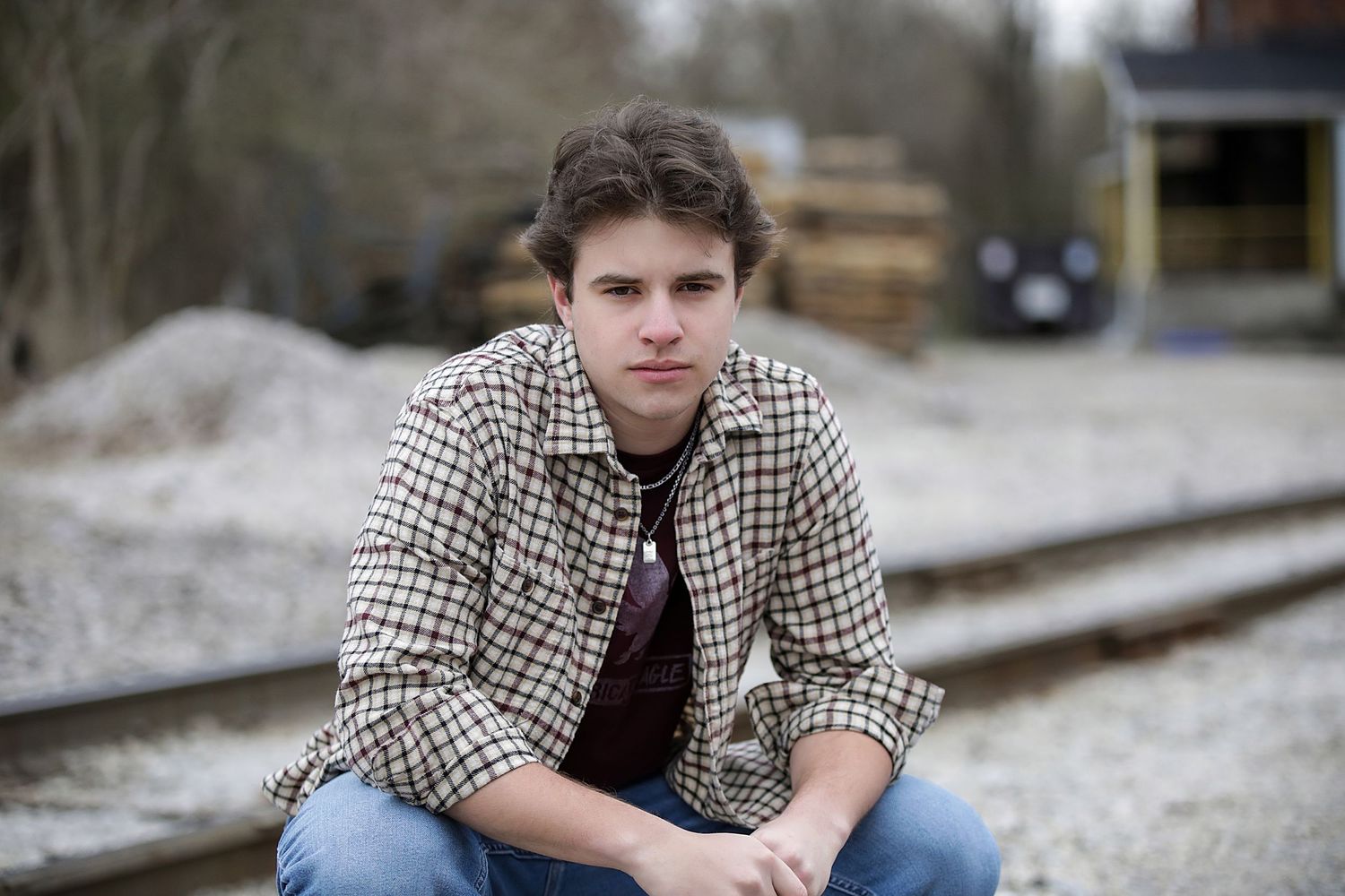 A person in a houndstooth jacket sits outdoors in a natural setting during winter.