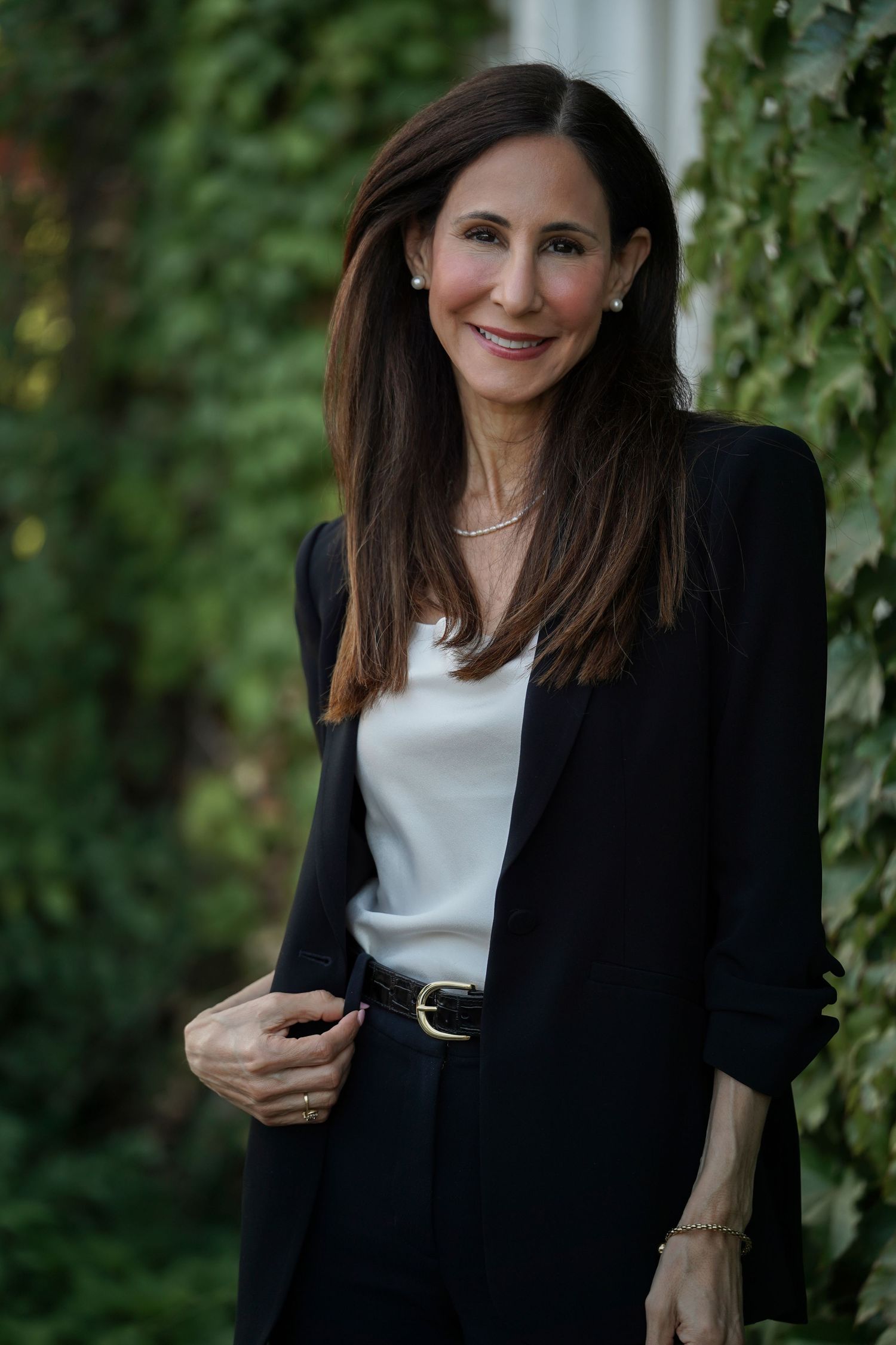 Professional portrait series shows a dark-haired woman in a black blazer and white top posing against leafy foliage backdrop.