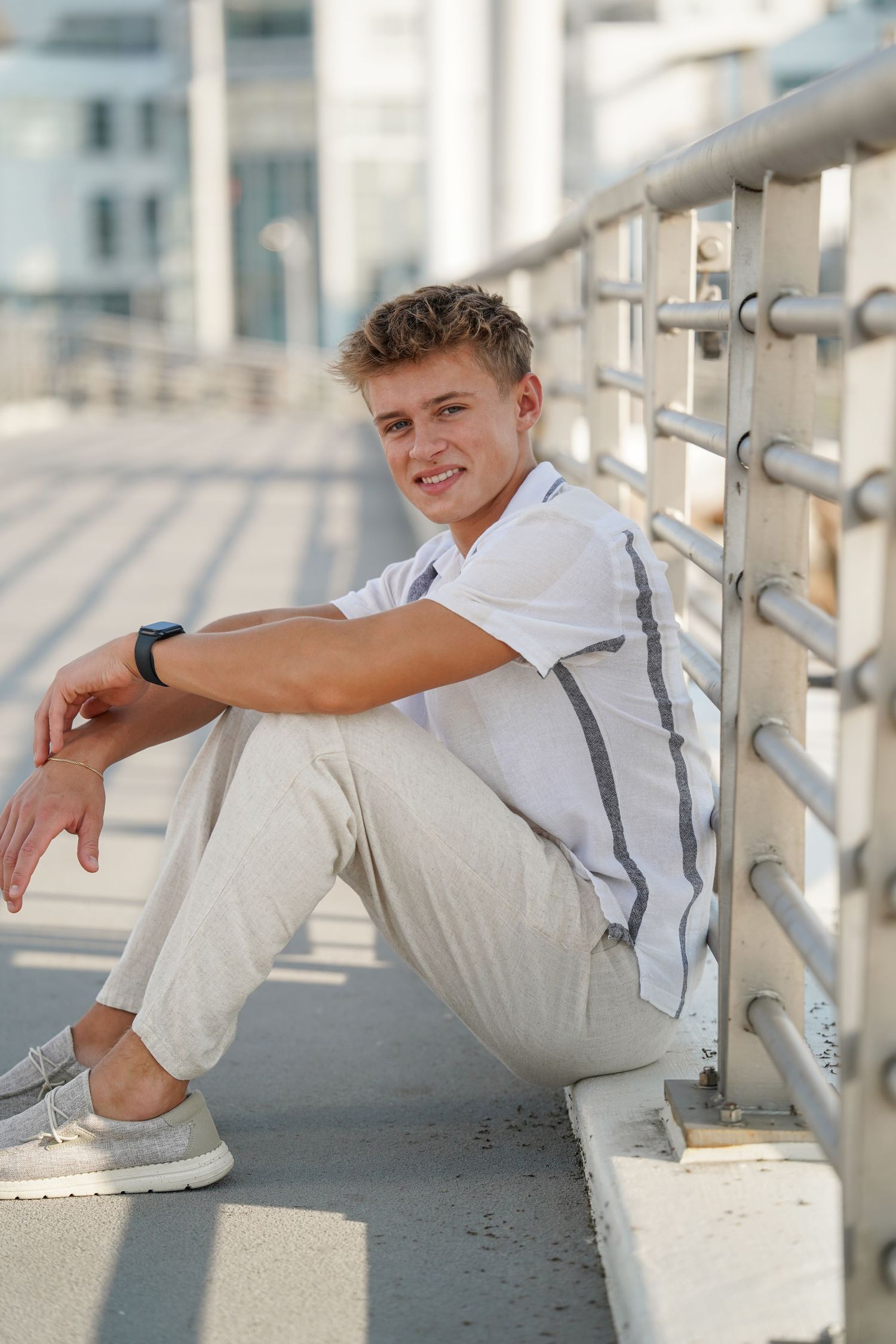 Person in casual white outfit leans against metal railing in bright natural lighting.